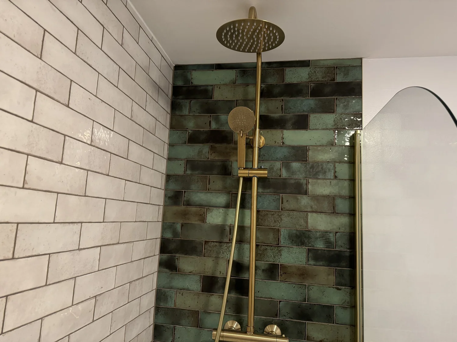 Modern shower with green and black tiles, brass fixtures and a rainfall showerhead