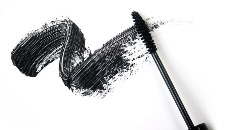 Black mascara wand applying mascara onto a white surface, creating a bold brushstroke.