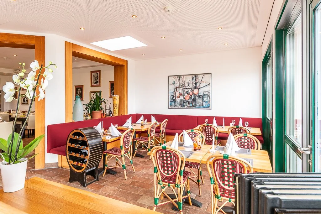 Ein Restaurant mit Tischen, Weingläser, und dekorativen Pflanzen sowie einem Wandbild.