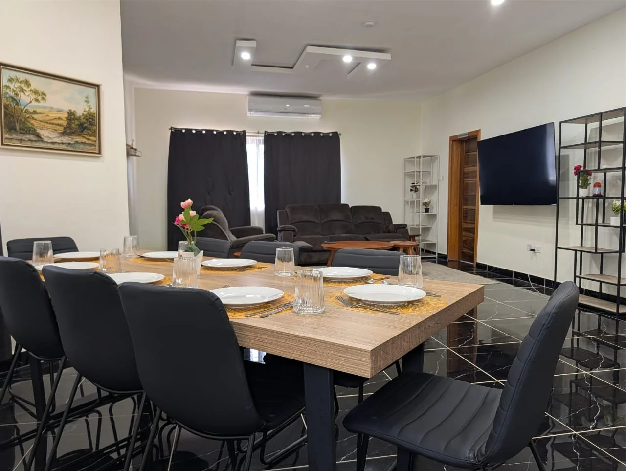 A bedroom with two twin beds, beige curtains, a wooden nightstand with a lamp, a small framed picture on the wall, and an open wooden wardrobe.