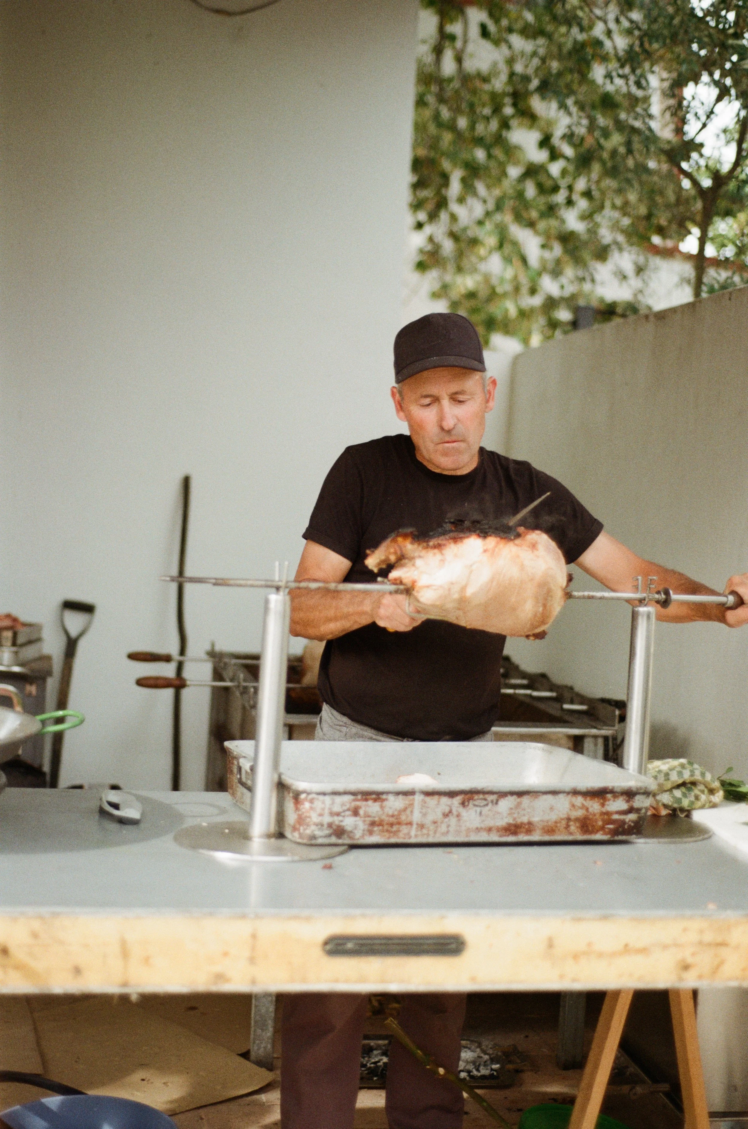 Homem assando um pernil de porco na churrasqueira ao ar livre.