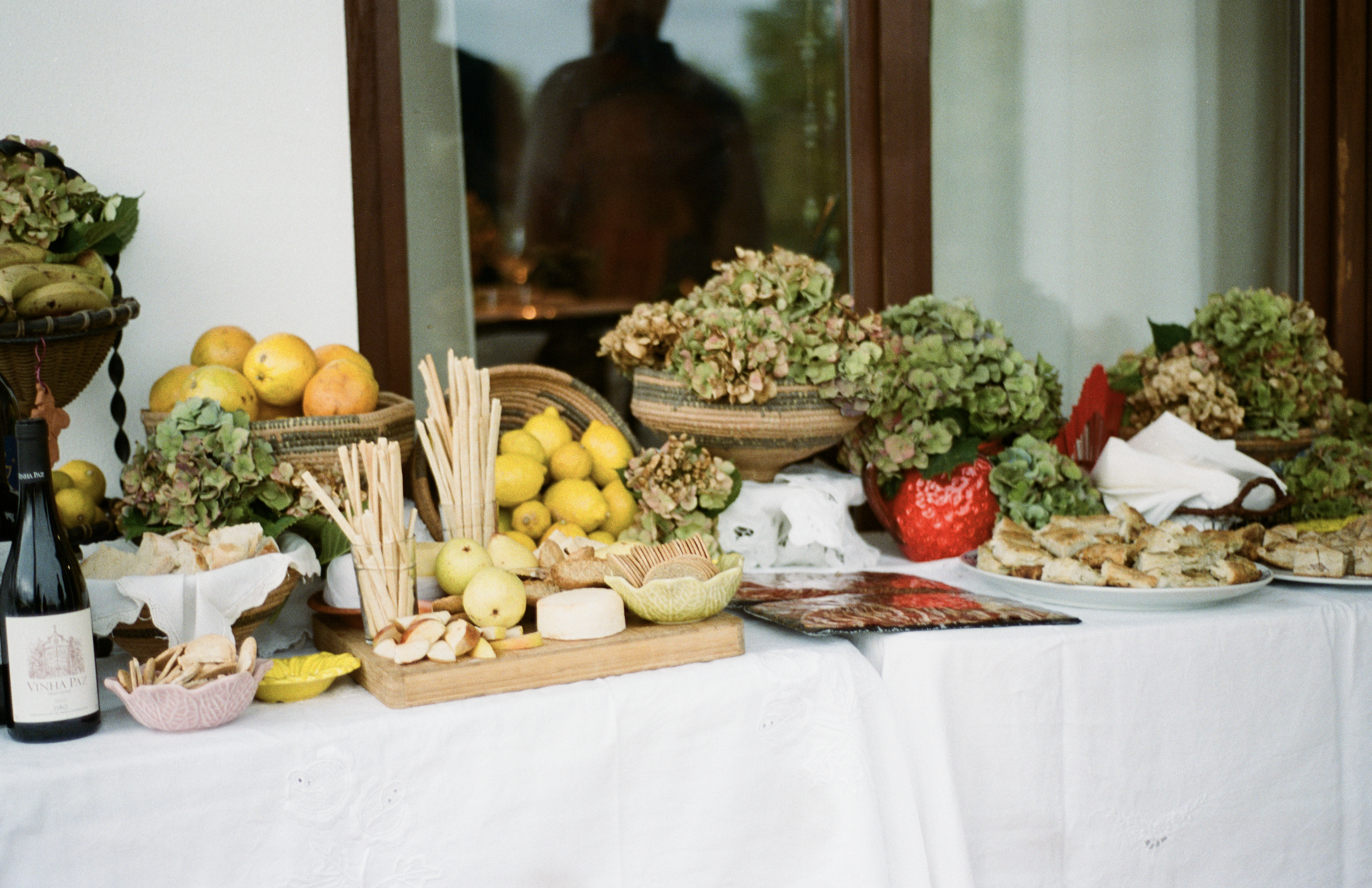 Mesa com frutas, plantas, queijos e alimentos em uma comemoração.