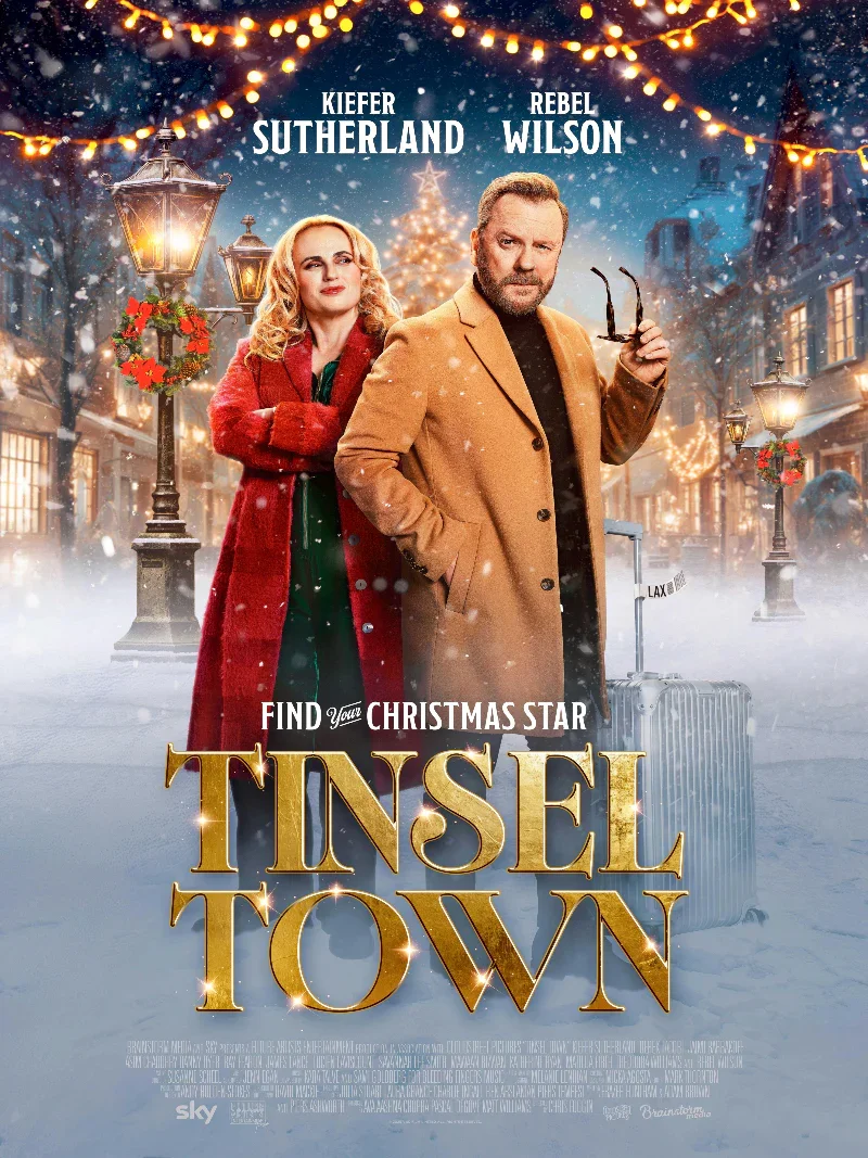 A Christmas-themed movie poster showing a man in a tan coat and glasses with a suitcase, and a woman in a red coat with blond hair, standing on a snow-covered street decorated with Christmas lights and wreaths. Behind them is a Christmas tree and his