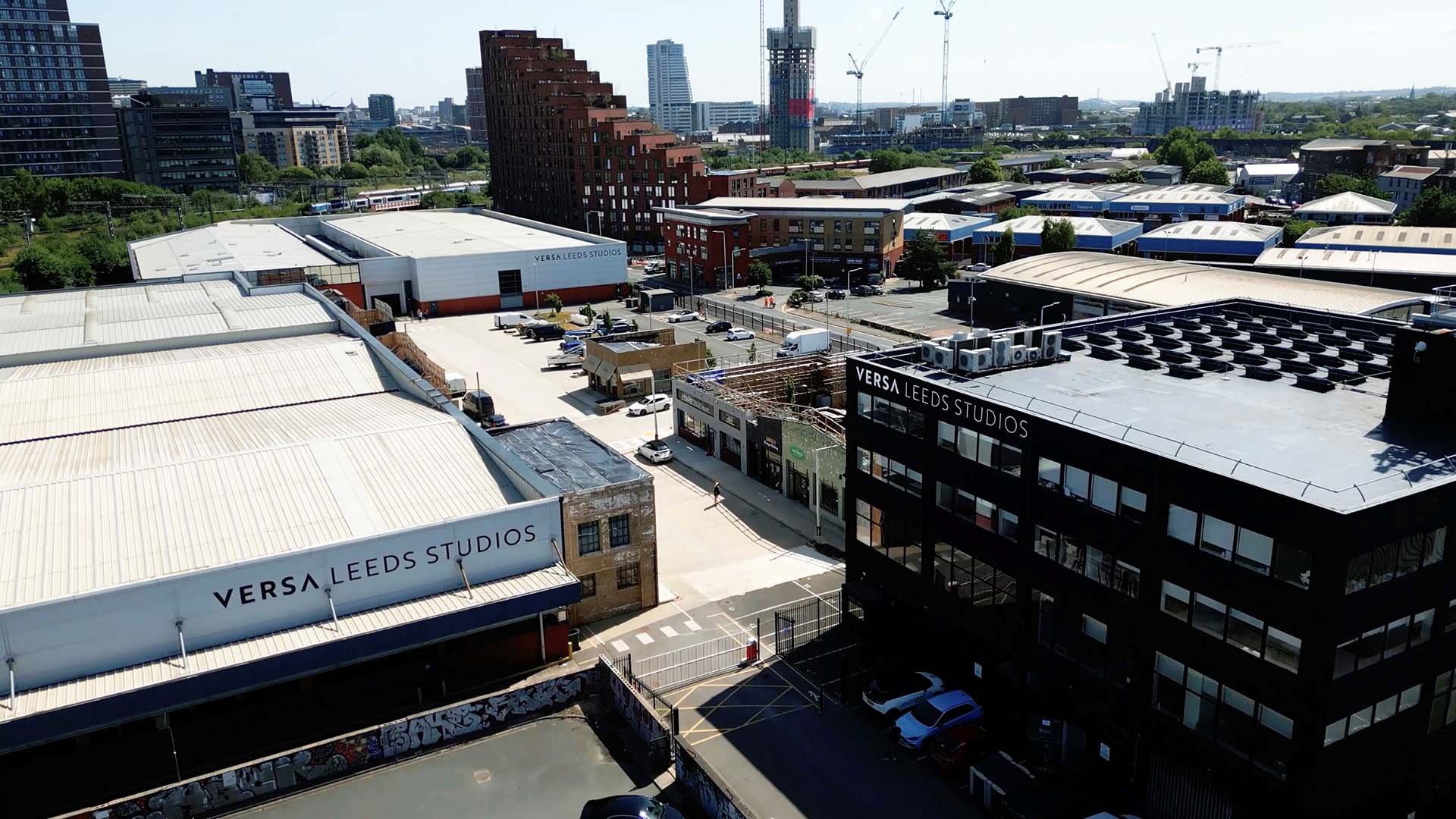 Aerial view of an urban cityscape with multiple buildings, including Versa Leeds Studios, construction cranes, and high-rise structures in the background.