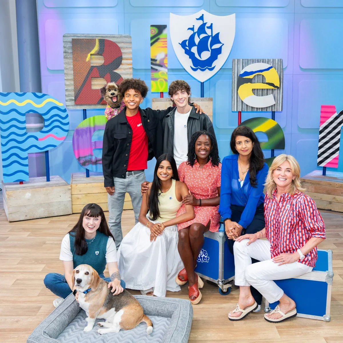 Group photo of ten people and two dogs in a colorful studio with large decorative letters and logos.