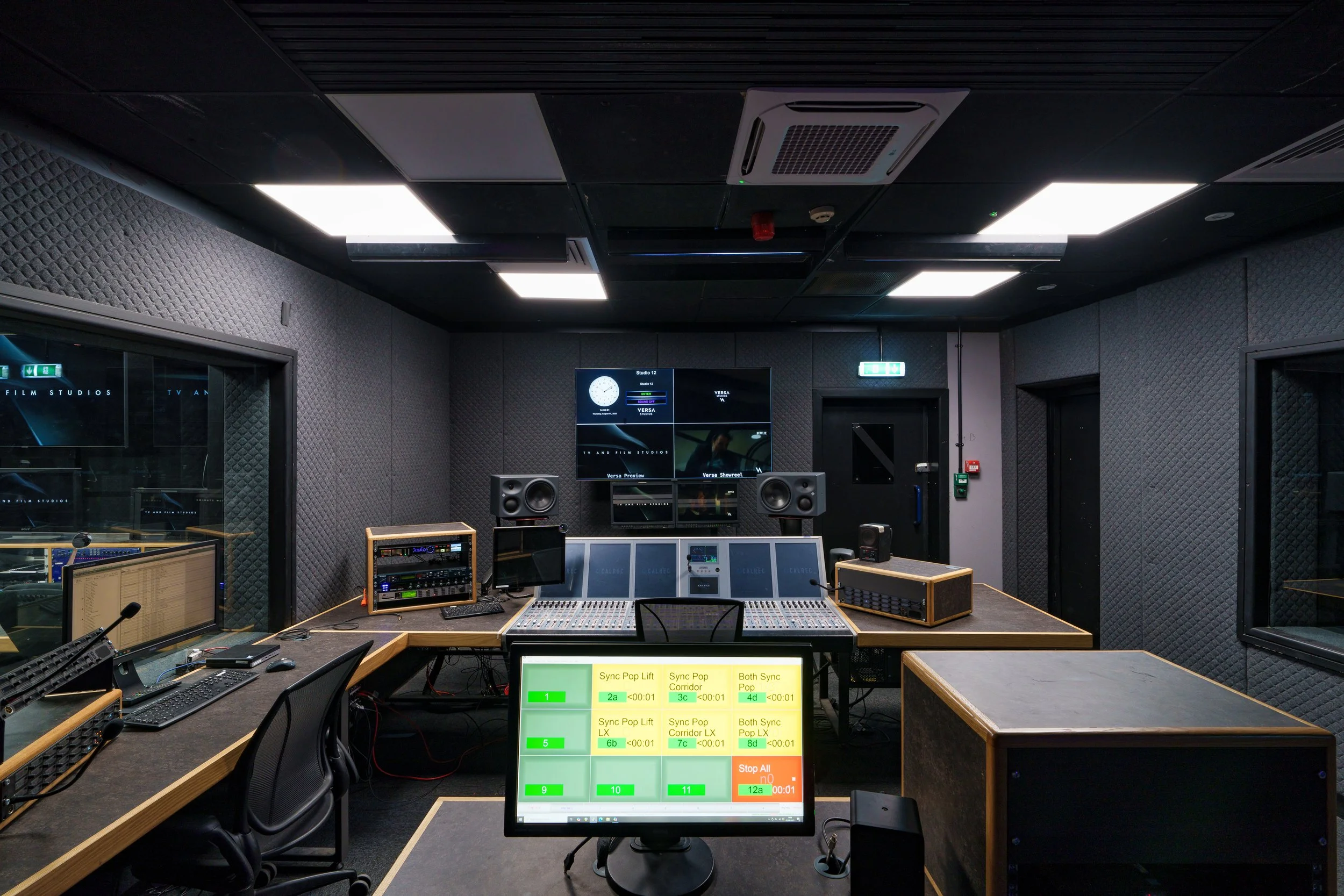 Recording studio control room with audio mixing console, multiple monitors, and soundproof walls, showing a control panel screen with various settings.