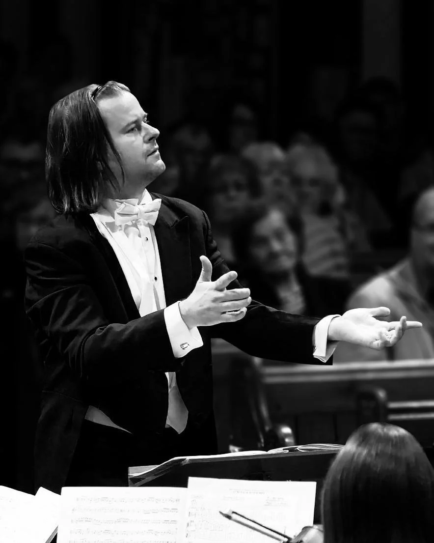 A conductor in formal attire leading an orchestra during a performance.