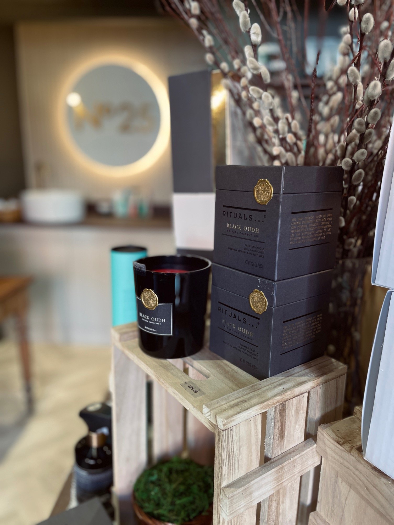 Display of Rituals Black Oudh scented candles and boxes on a wooden shelf with a potted plant below, in a retail store.