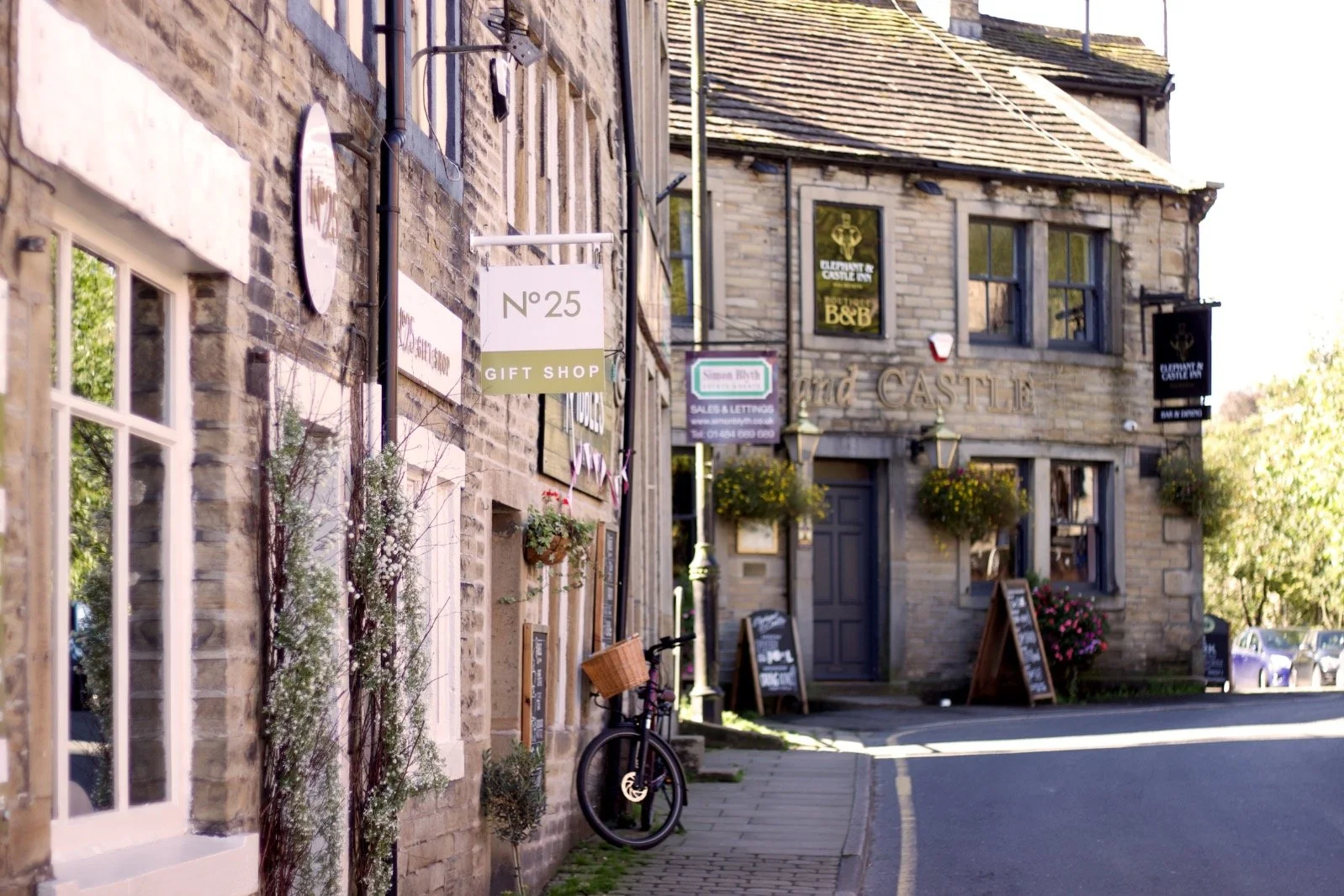 A street view of a charming stone building with signs for a gift shop, a bar, and a bed and breakfast, with flower baskets and a bicycle parked on the sidewalk.
