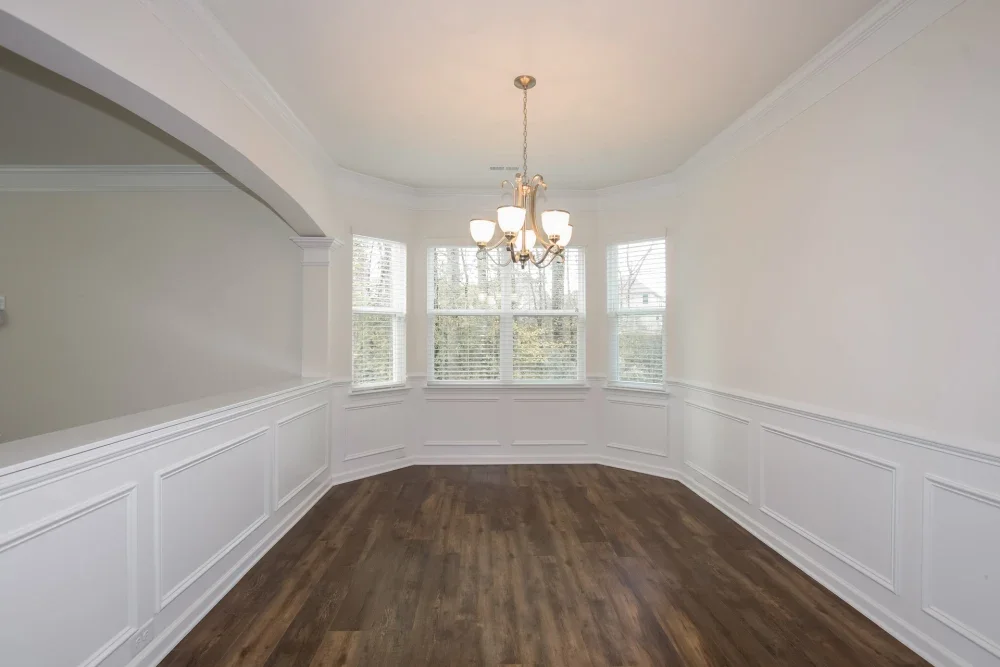 Empty dining room with hardwood floors, white wainscoting, large bay windows, and a chandelier.