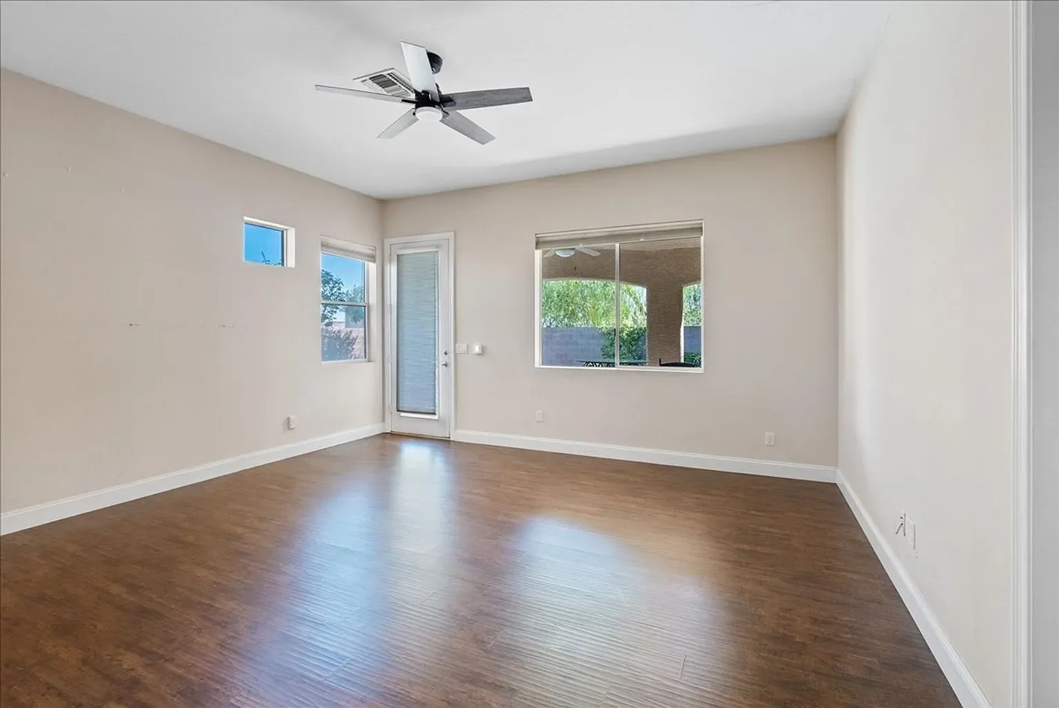 Empty room with wood flooring, two windows, a glass door leading outside, a ceiling fan, and neutral-colored walls.