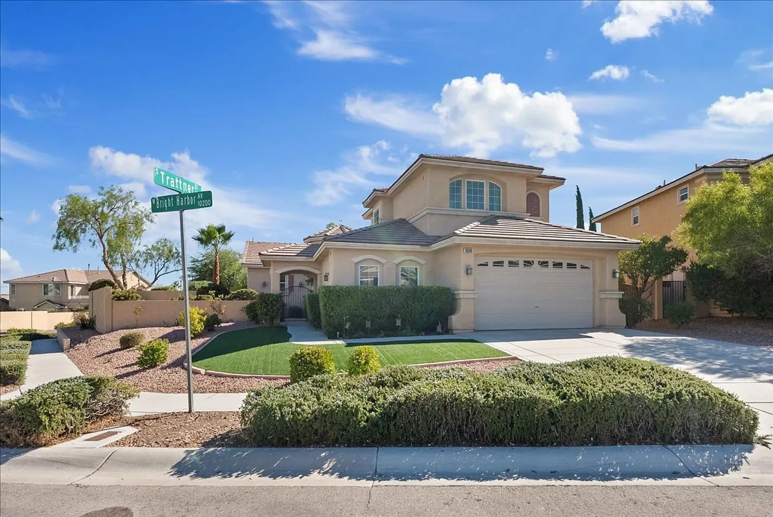 A two-story house with a manicured lawn and bushes, located on a corner lot at the intersection of Trattner Street and Bright Harbor Avenue under a partly cloudy blue sky.