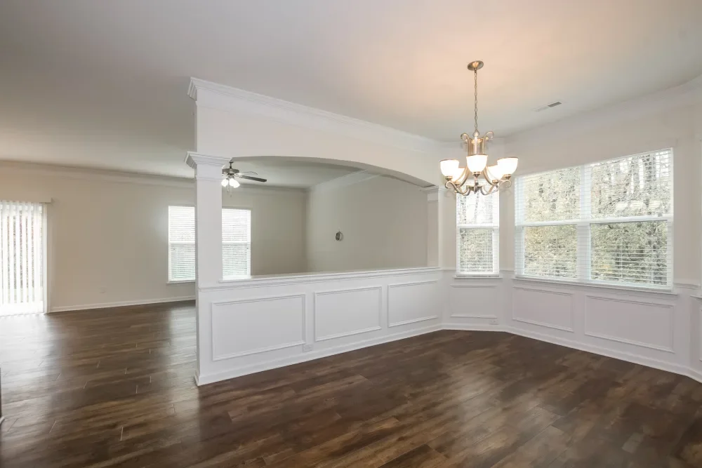 Empty dining room with hardwood floors, large windows with blinds, and a chandelier hanging from the ceiling.