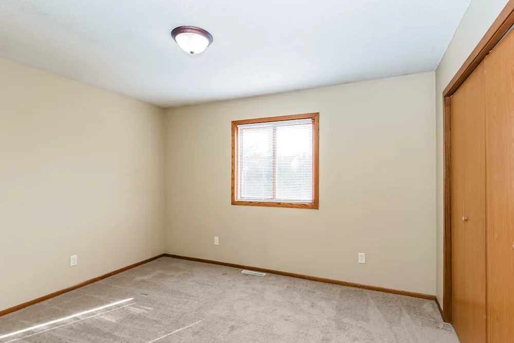 Empty bedroom with beige walls, a window with blinds, a closet door, and carpeted floor.