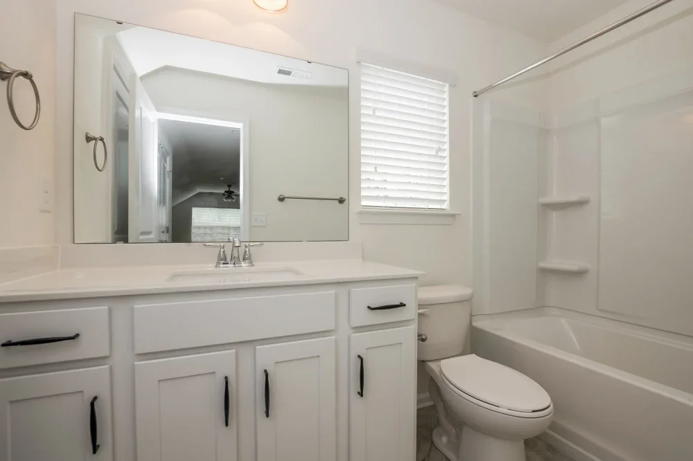White bathroom with vanity, mirror, toilet, and bathtub with shower area and built-in shelves.