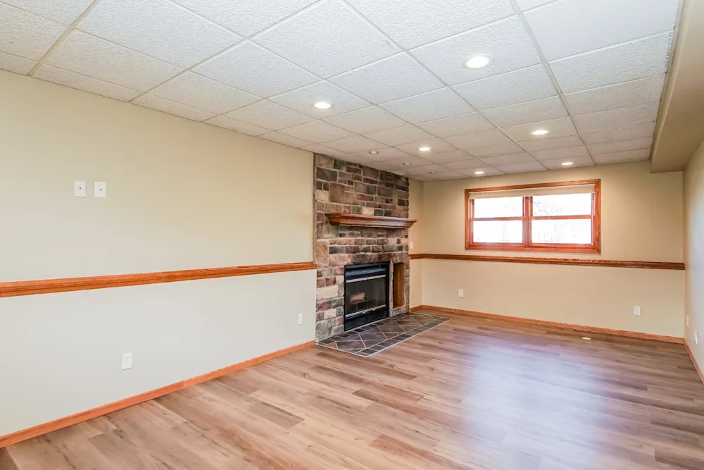 Empty living room with a brick fireplace, wooden trim, a window, and hardwood floors.