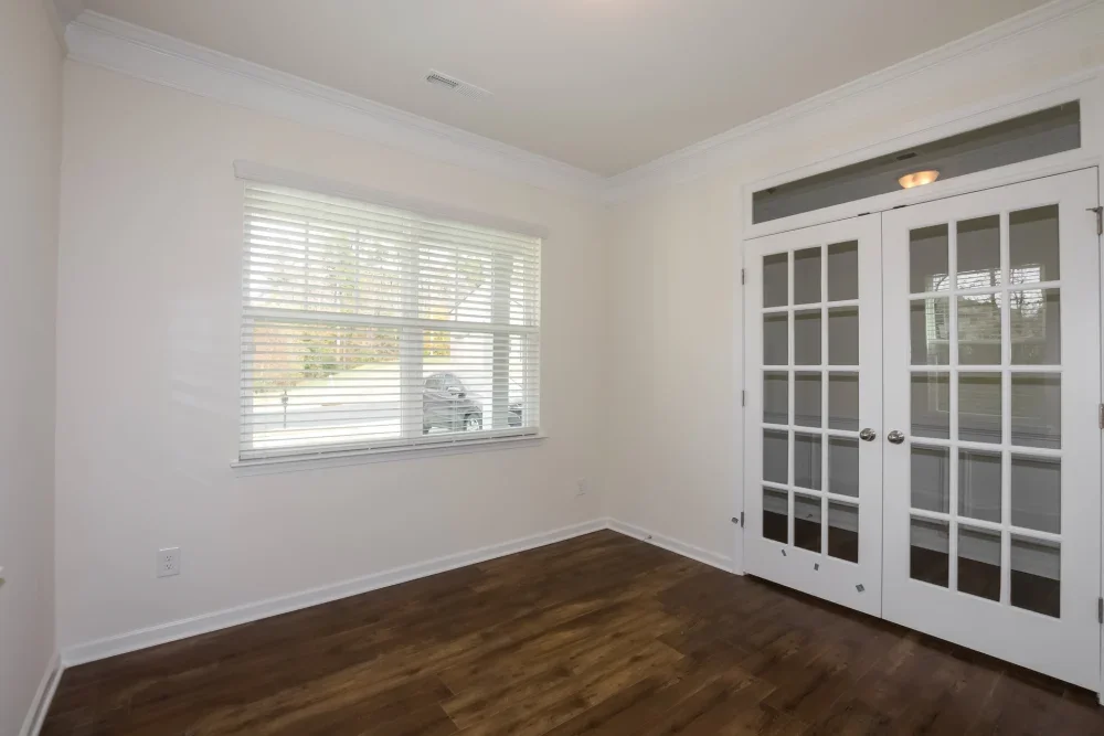 Empty room with hardwood floors, white walls, a window with blinds, and a set of French doors with glass panels.