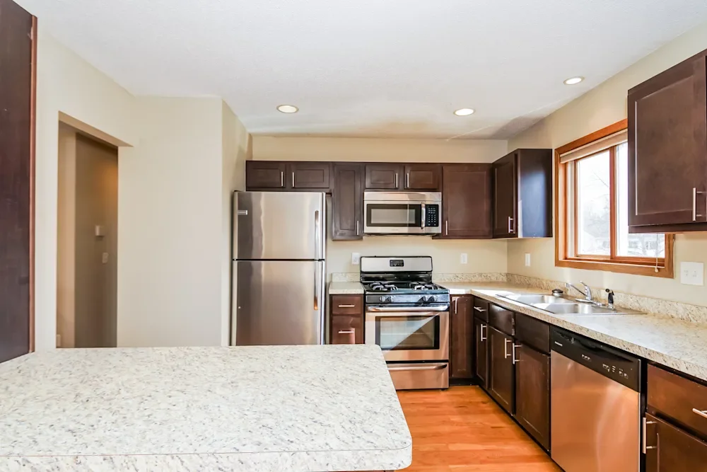 Kitchen with stainless steel refrigerator, microwave, oven, dishwasher, dark wood cabinets, granite countertops, and a window above the sink.