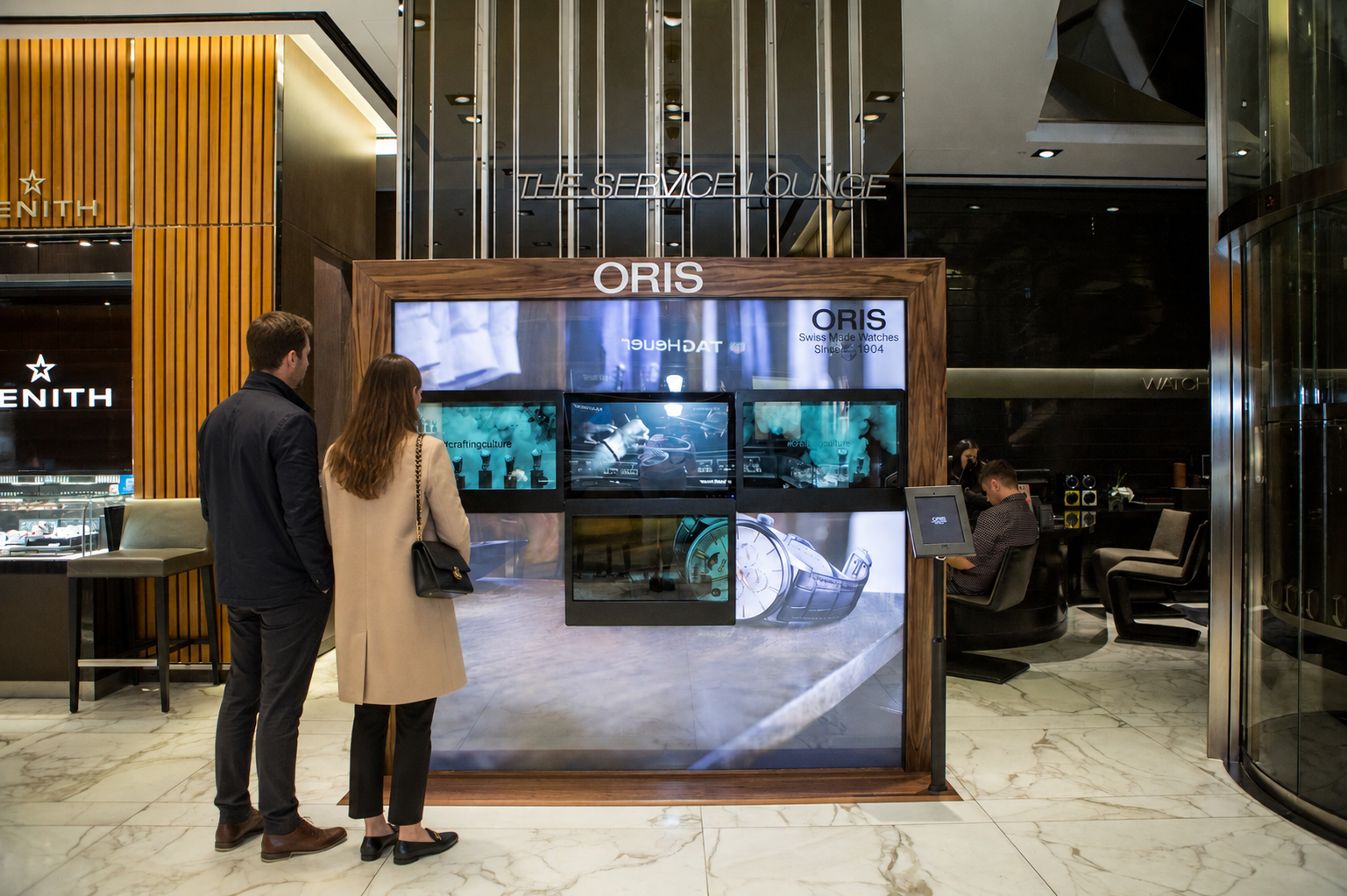 A man and a woman standing in front of an Interactive ORIS watch display at a store.