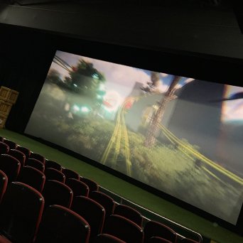 A large movie theater screen displaying a scene with tracks and trees, with red theater seats in front.