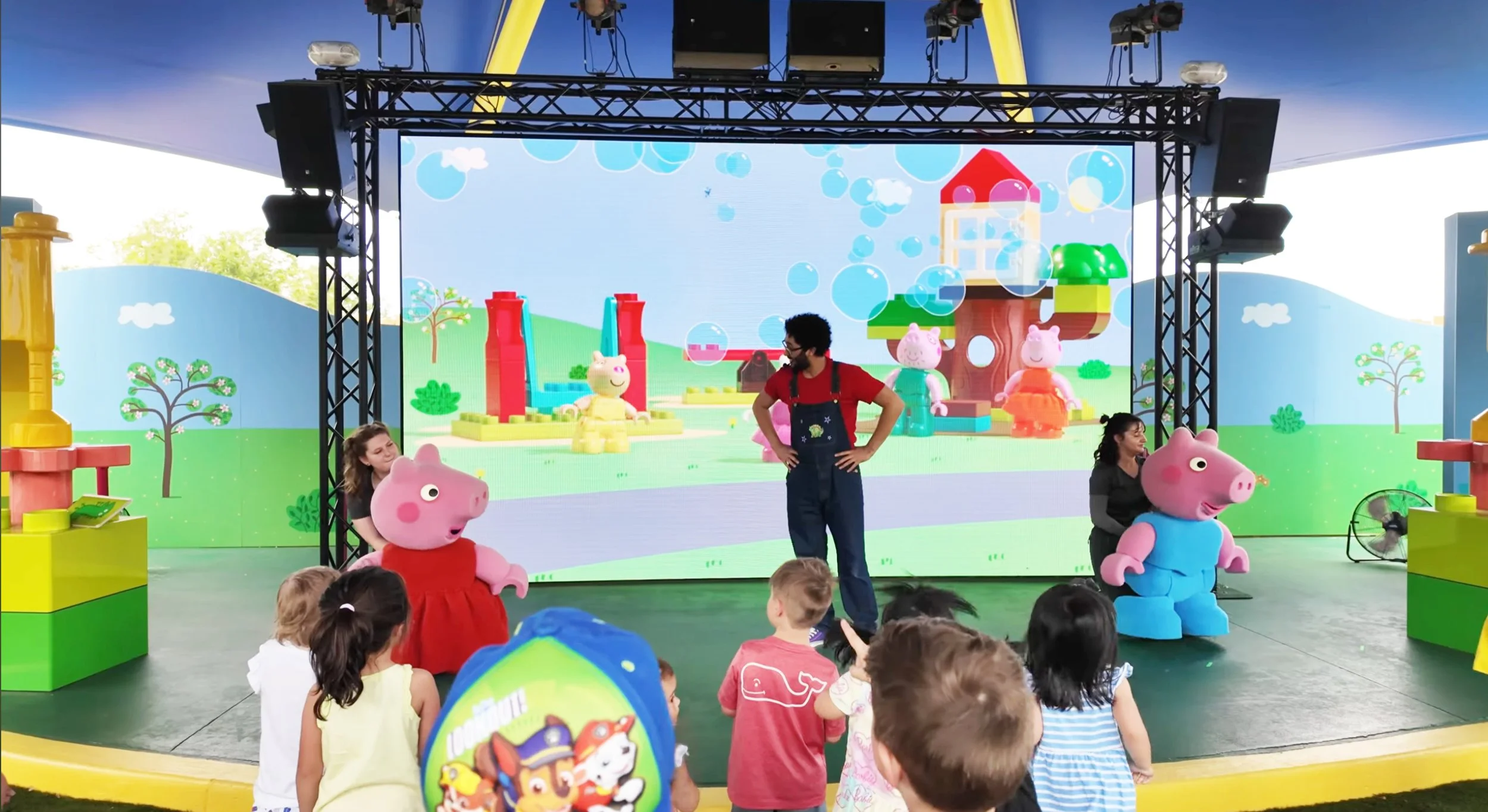 Children watching a Theatre  performance with characters from Peppa Pig, including Peppa in a red dress and George in a blue outfit, at Legoland Playdate with Peppa and George Theatre Billund Parachute studios