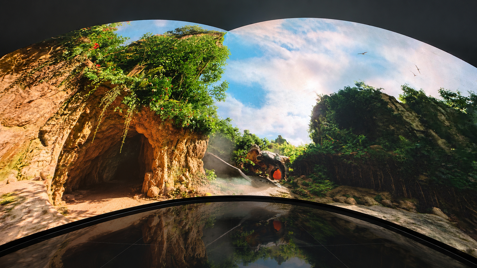 A panoramic view of a themed dinosaur ride with rocky cave tunnels and lush green foliage, 270 immersive LED dome Parachute Studios
