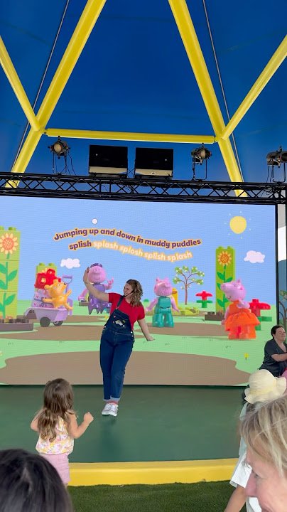 Children watching a woman perform on an outdoor Theatre with a Peppa Pig themed screen in the background. Playdate with Peppa and George Theatre Legoland New York Parachute studios
