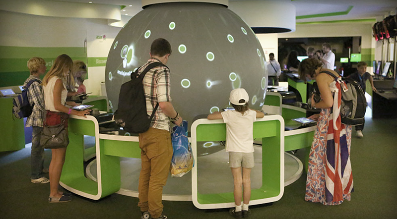 Children and adults gathered around a spherical digital display in a tech exhibit.