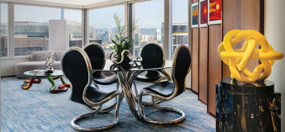 Marriot Hotel Suite Modern office dining area with a glass table, black and chrome chairs, abstract artwork on the wall, sculpture on a pedestal, and city view outside windows.