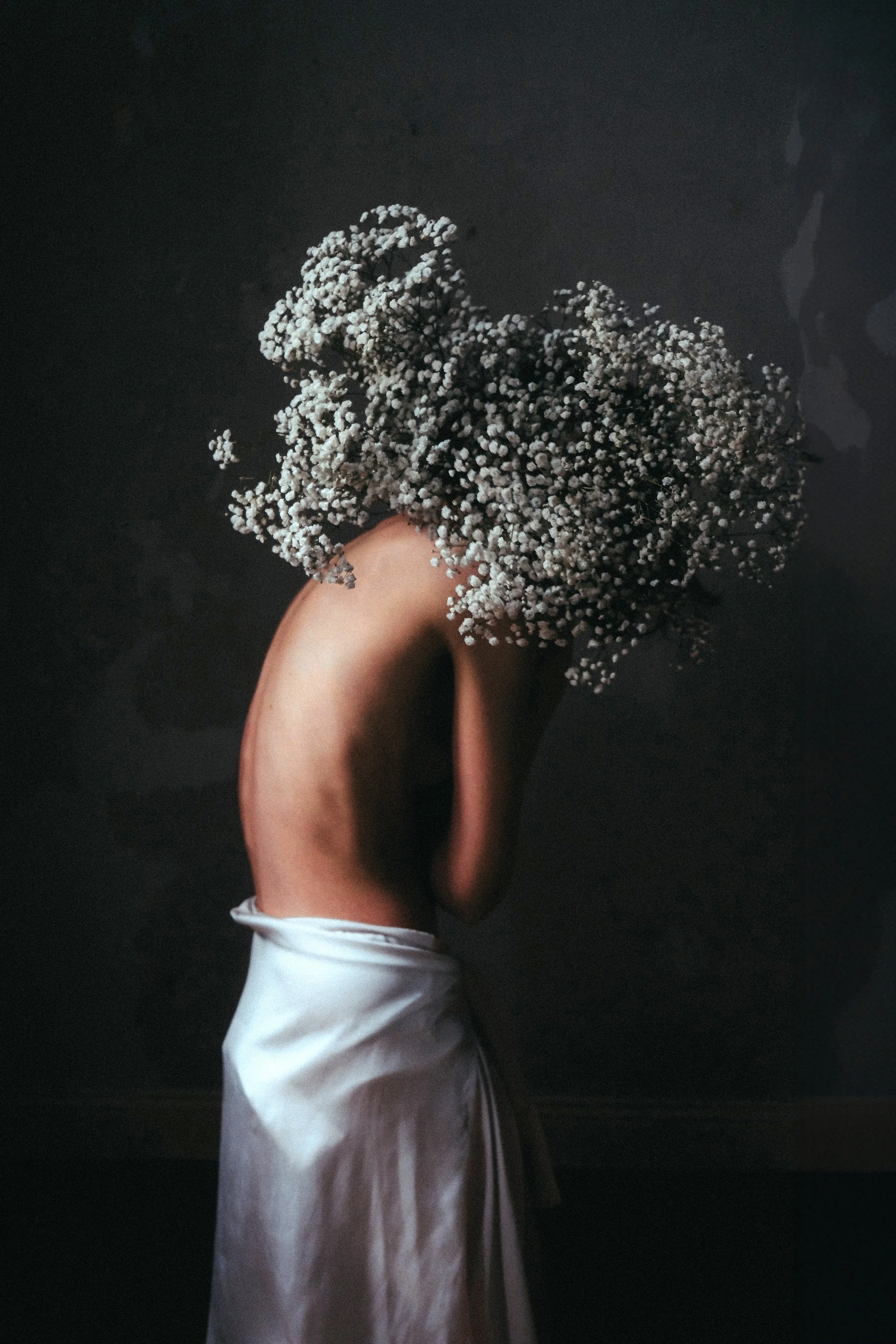 Eine kreative Fotografie einer nackten Person, die den Rücken zeigt, mit einem großen, schwarzen, lockigen Haarbüschel, der wie eine Blume aussieht, und einem weißen Kleidungsstück um die Hüften.