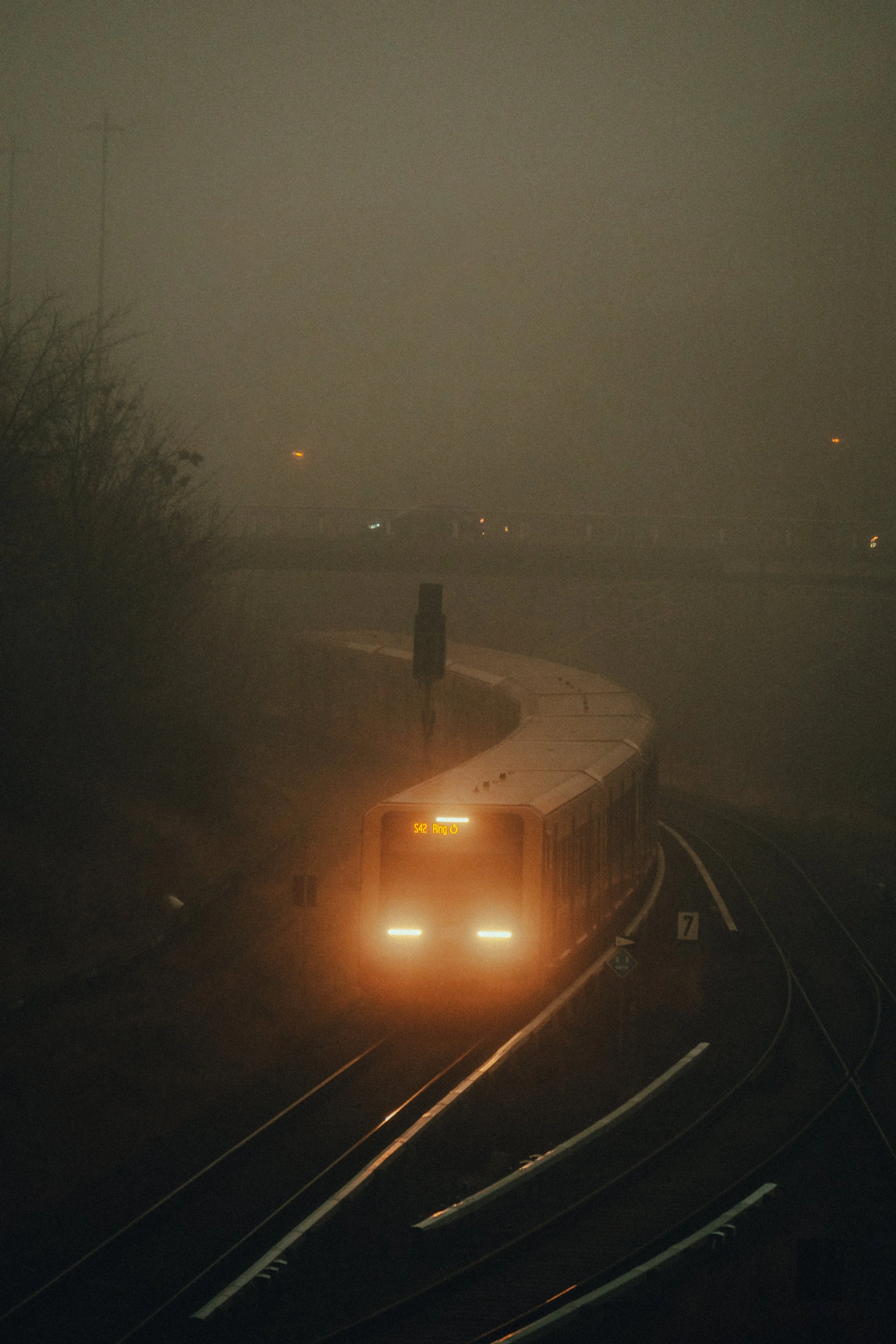 Ein Zug fährt durch nebliges Wetter bei Nacht auf einer kurvigen Bahnstrecke.