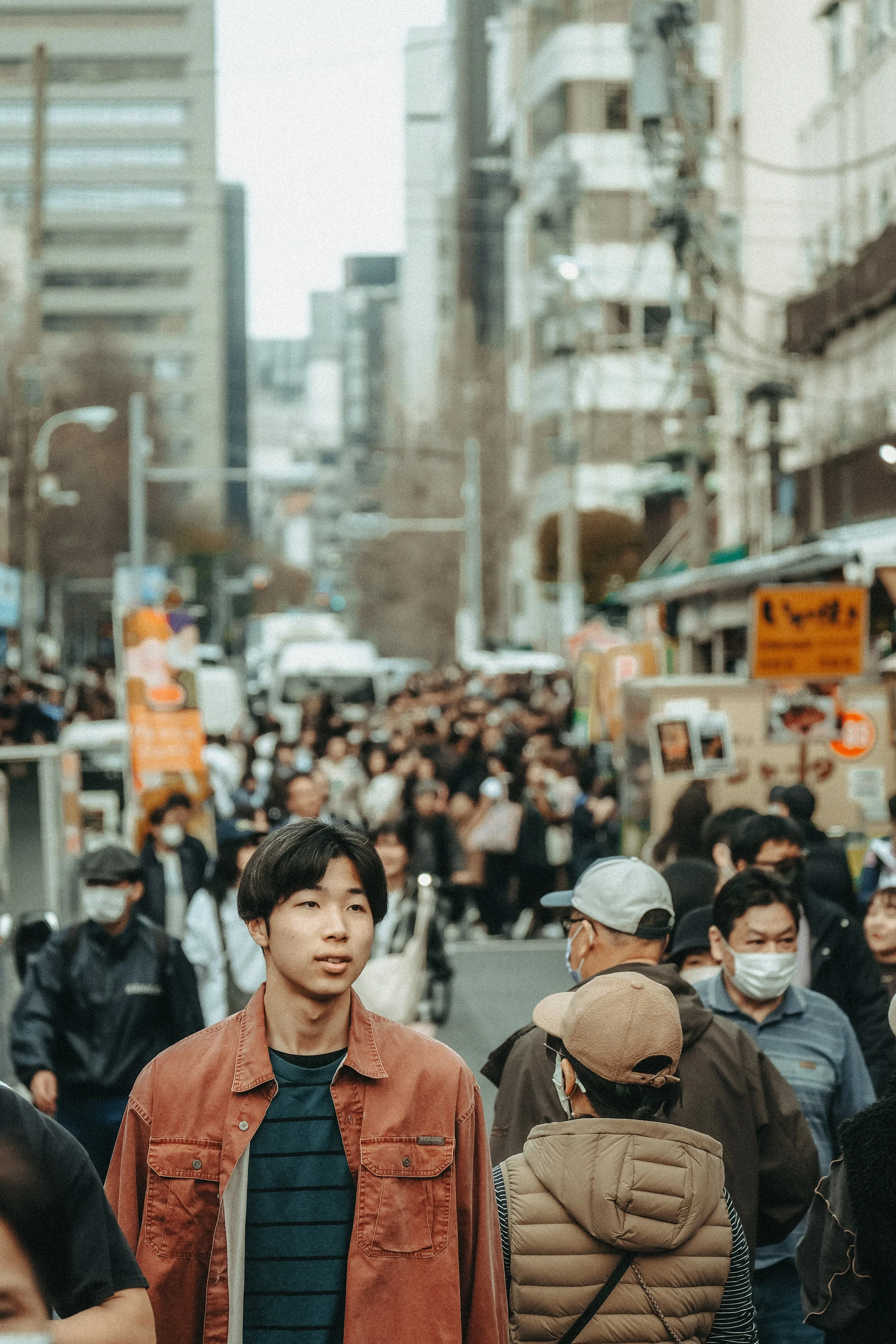 Menschen drängeln sich auf einer belebten Stadtstraße, viele tragen Gesichtsmasken.