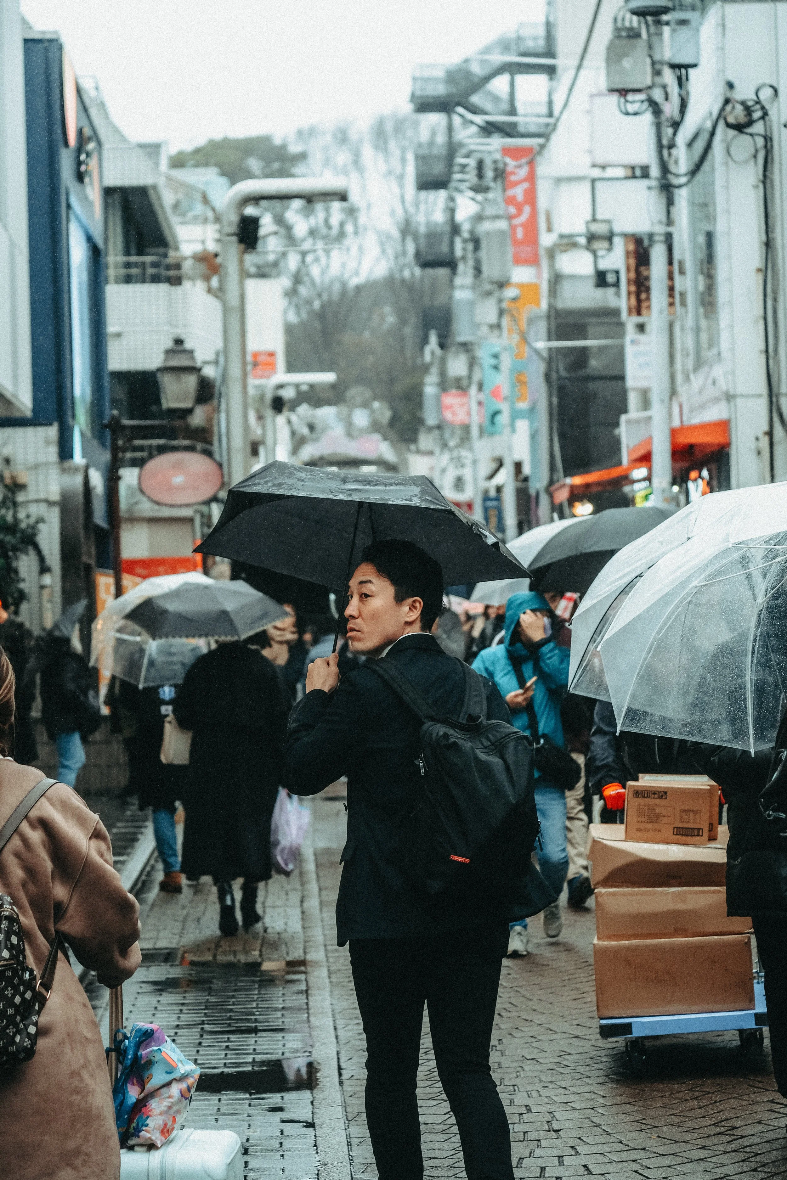 Menschen mit Regenschirmen in einer belebten Straße, im Hintergrund Gebäude und Geschäfte