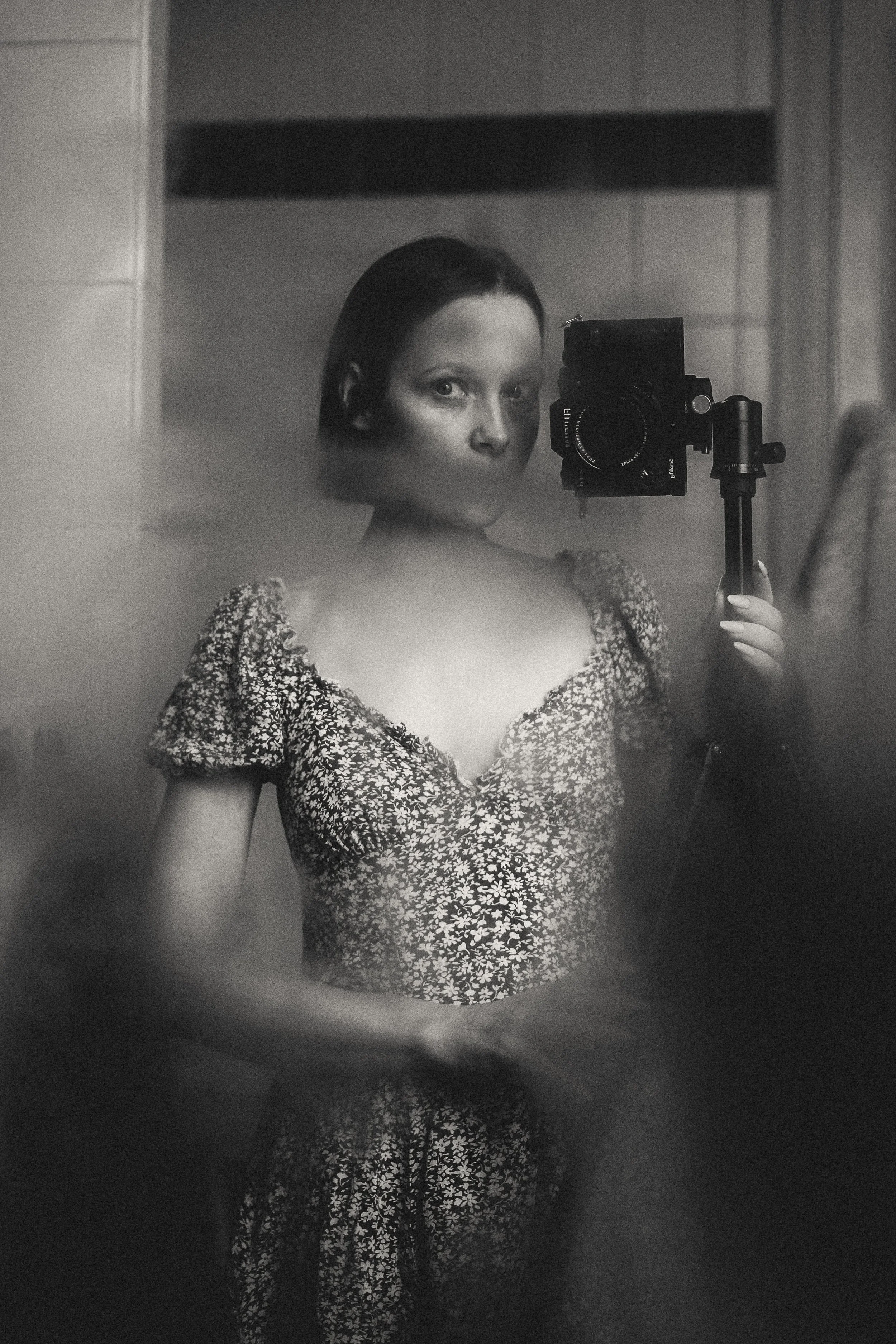 Schwarz-Weiß-Foto einer jungen Frau, die eine Kamera vor einem Spiegel hält und ein Foto von sich selbst macht.