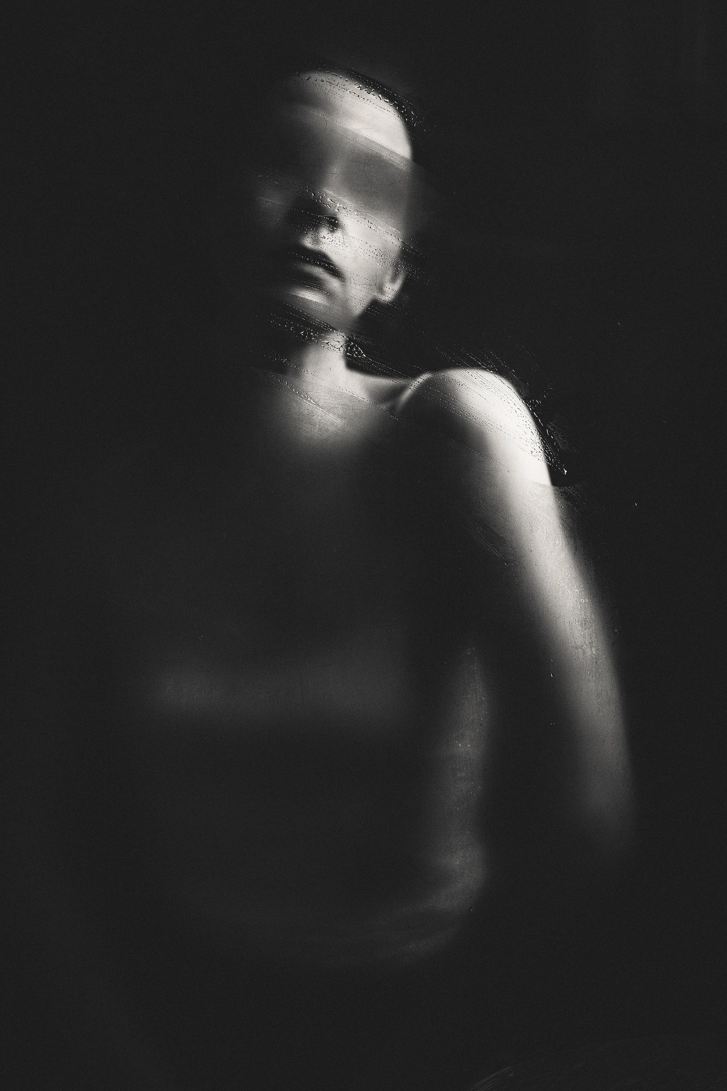 Schwarz-weiß-Foto eines Angebots, eines Menschen, der sich an eine scheibe oder Wand lehnt, mit Wassertröpfchen auf der Oberfläche.