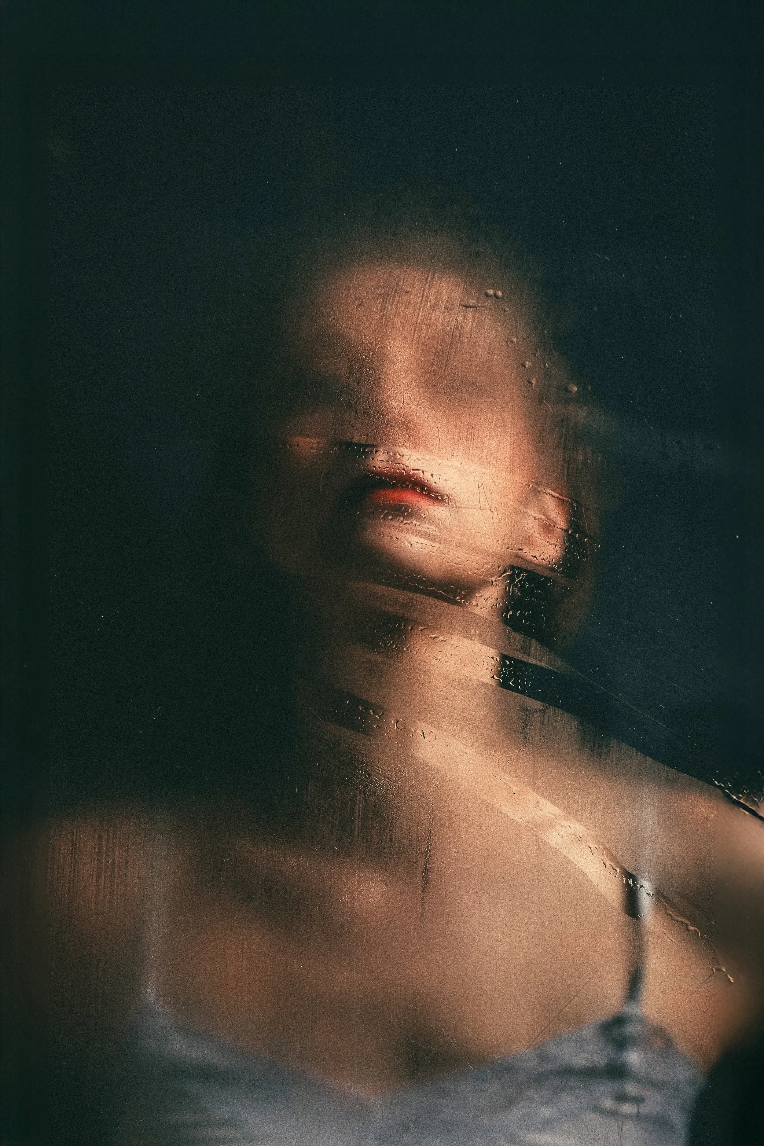 Nebelnde Fensterscheibe mit Sicht auf eine halb verdeckte Frau, deren Gesicht unscharf ist, durch Wassertröpfchen auf der Glasscheibe