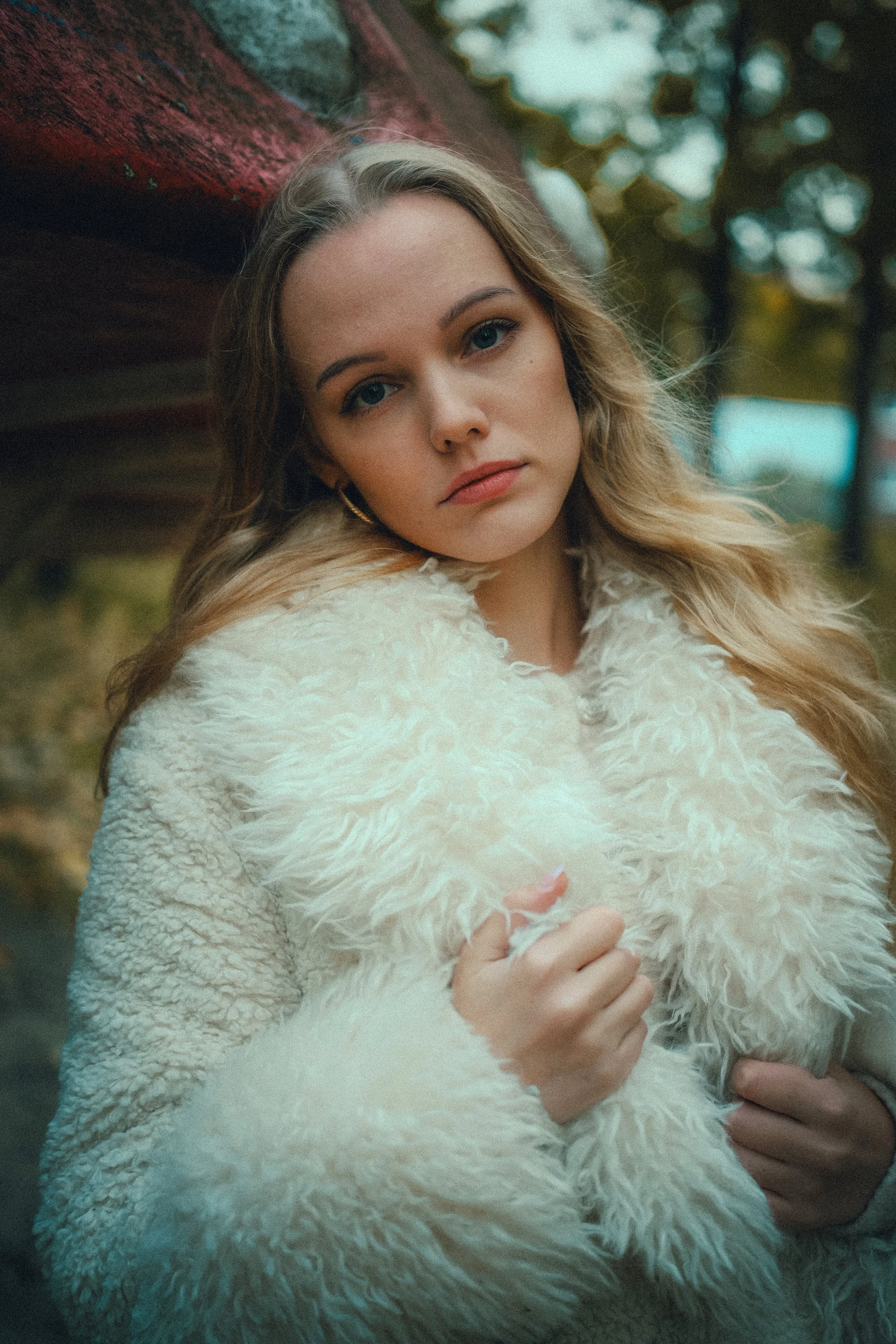 Junge Frau mit blondem Haar in weißem Pelzmantel outdoor, unscharfer Herbsthintergrund.