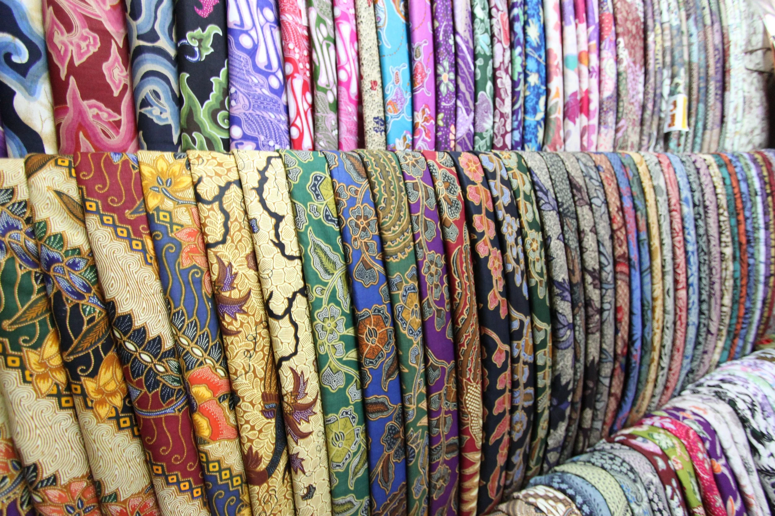 Colorful fabric rolls with various intricate patterns and designs, arranged on shelves.
