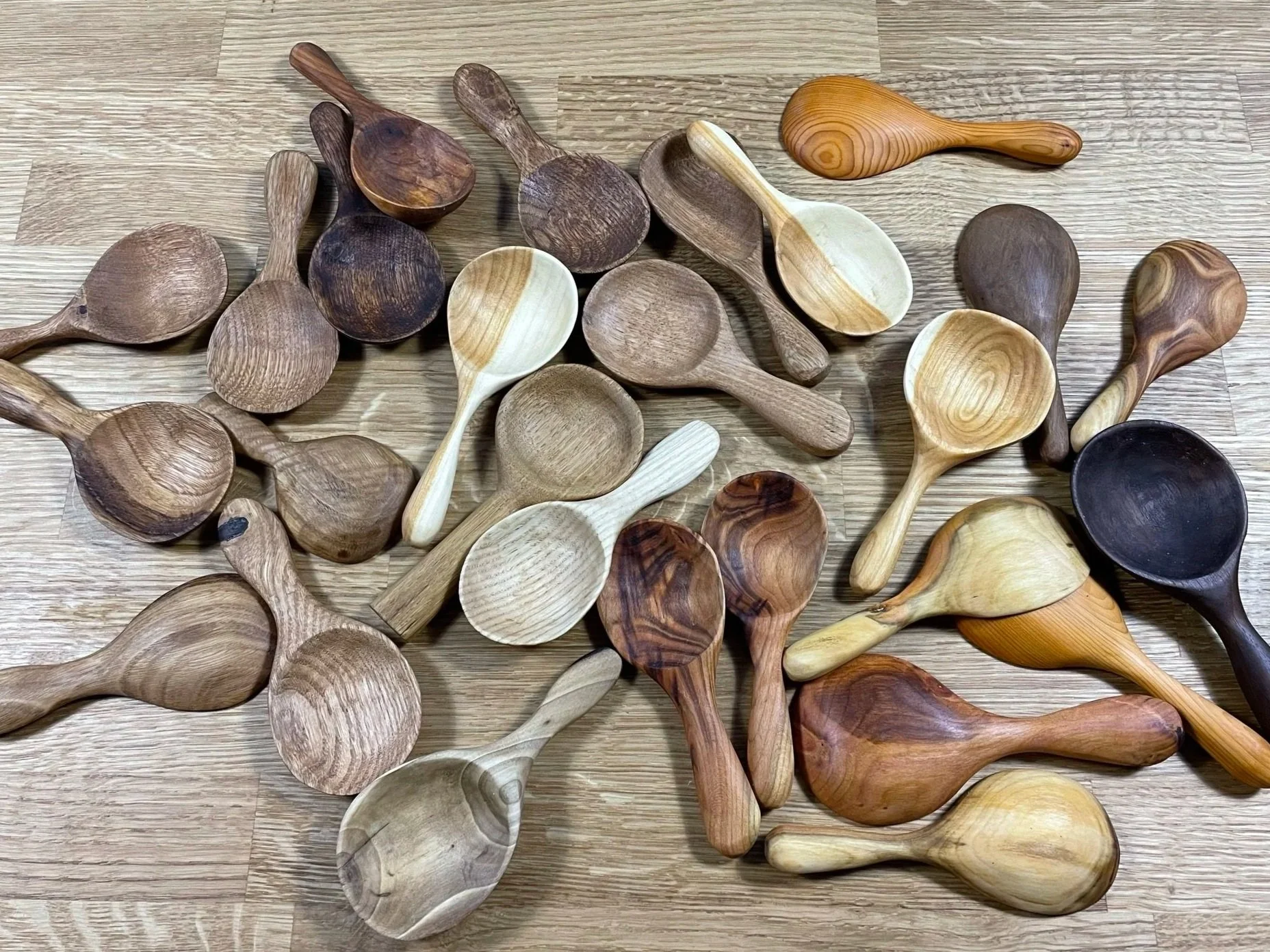 A collection of various wooden spoons in different sizes, shapes, and wood types laying on a wooden surface.