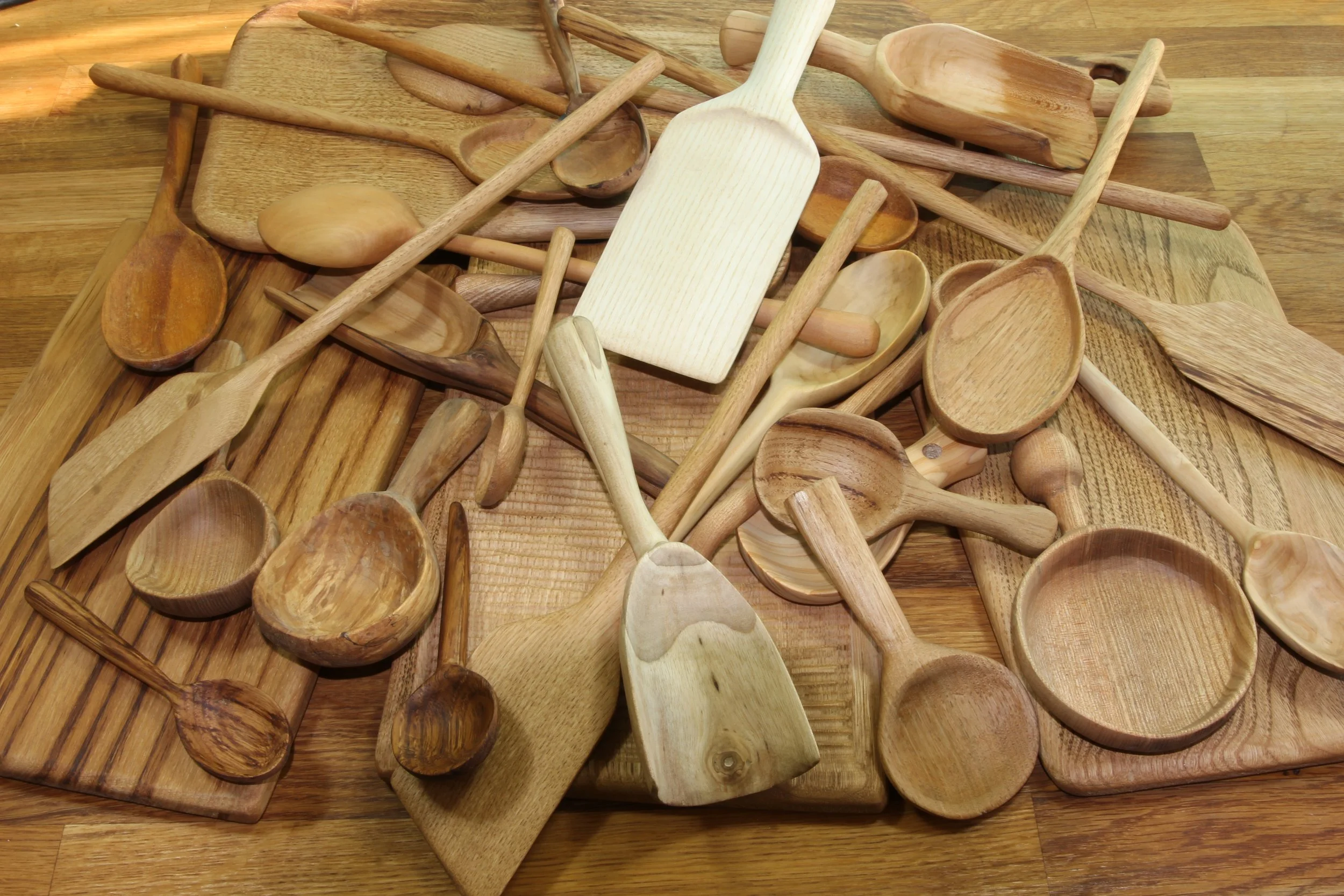 A collection of various wooden kitchen utensils, including spoons, spatulas, and cutting boards, scattered on a wooden surface.