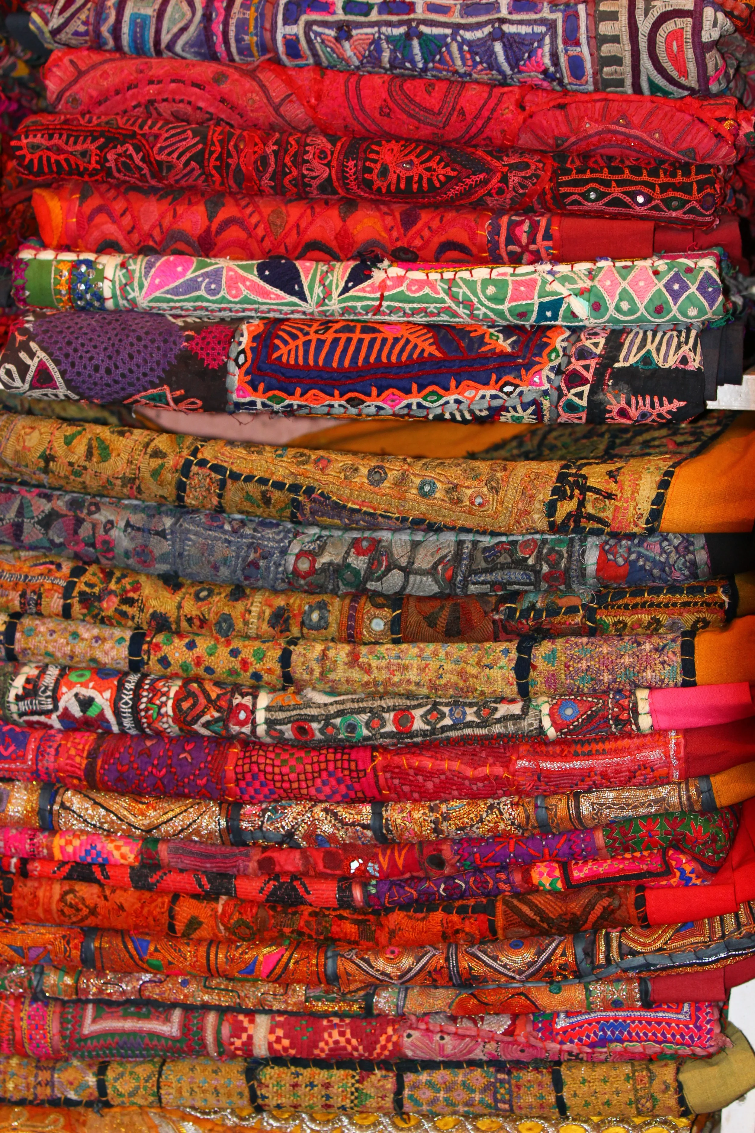 Stack of colorful, embroidered textiles with intricate patterns and designs.