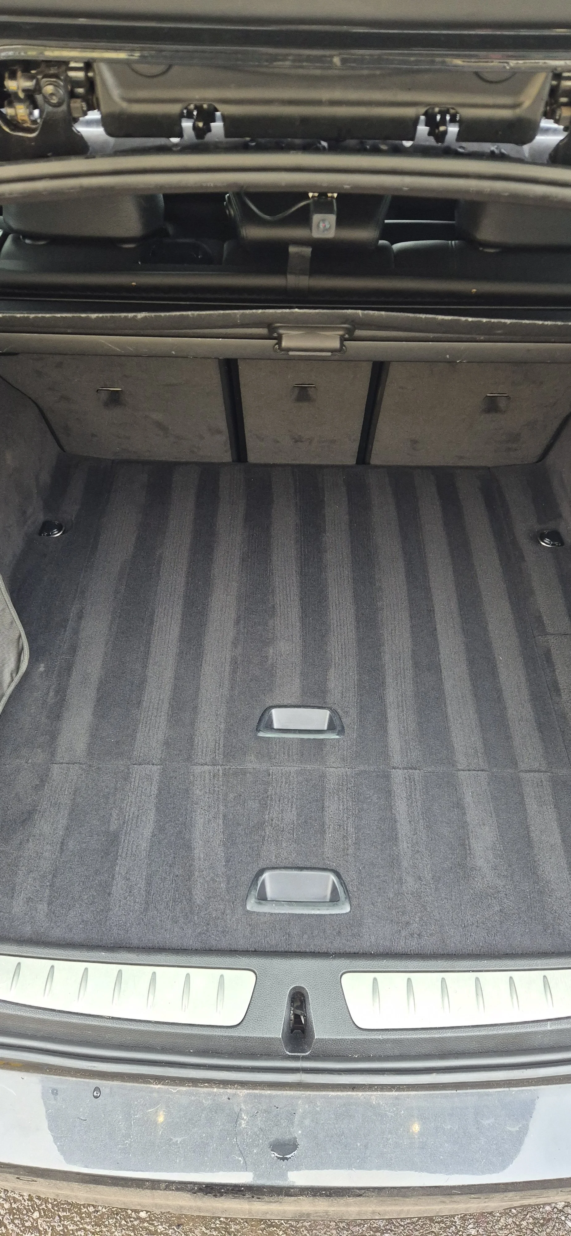Empty car trunk with folded seats and carpeted floor with two handles.