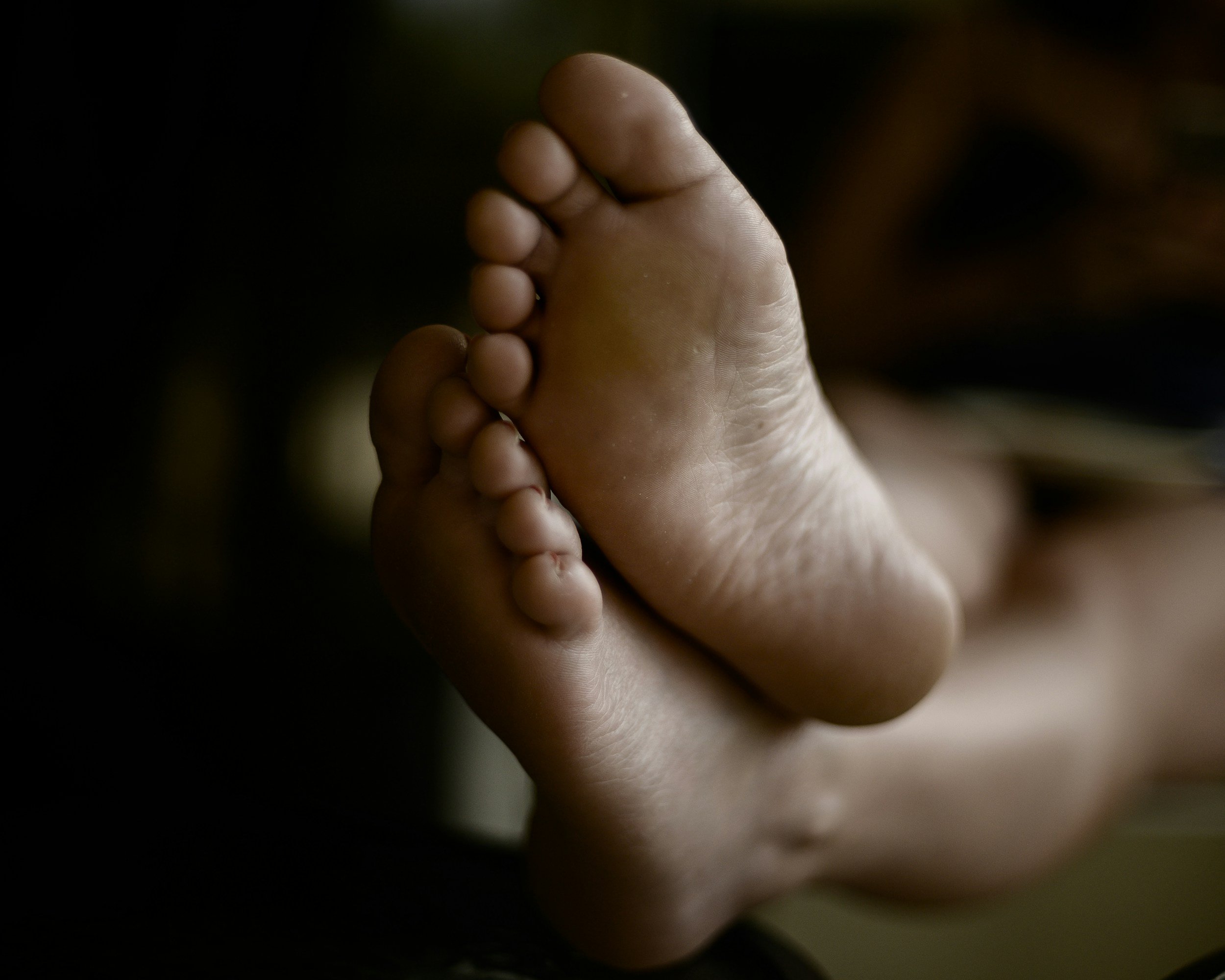 Black and white photo of bare feet with soles facing upward, isolated against a dark background.