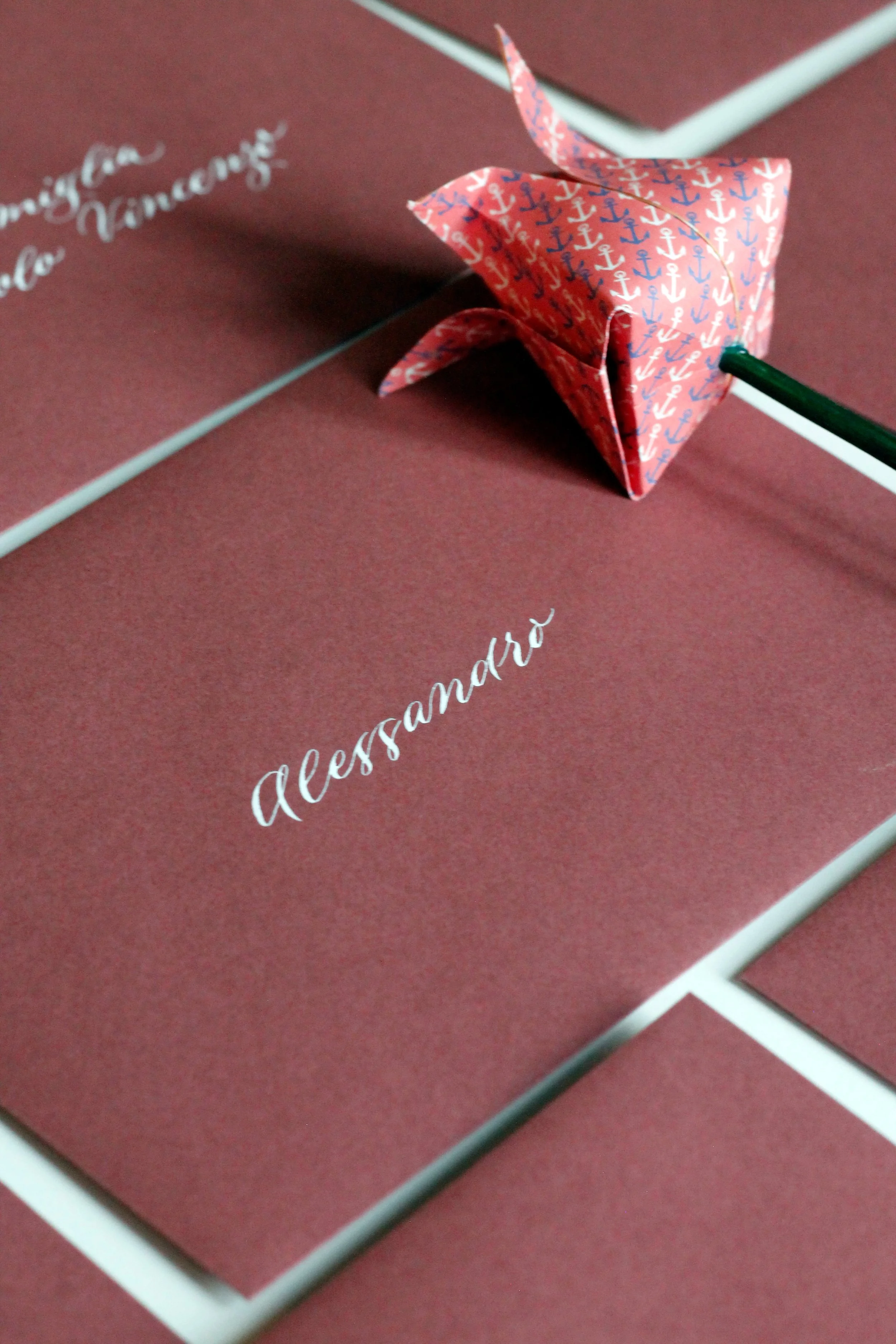 Carta di invito con nome 'Alessandro' e biglietto con fiore di carta decorato con un motivo a ancore