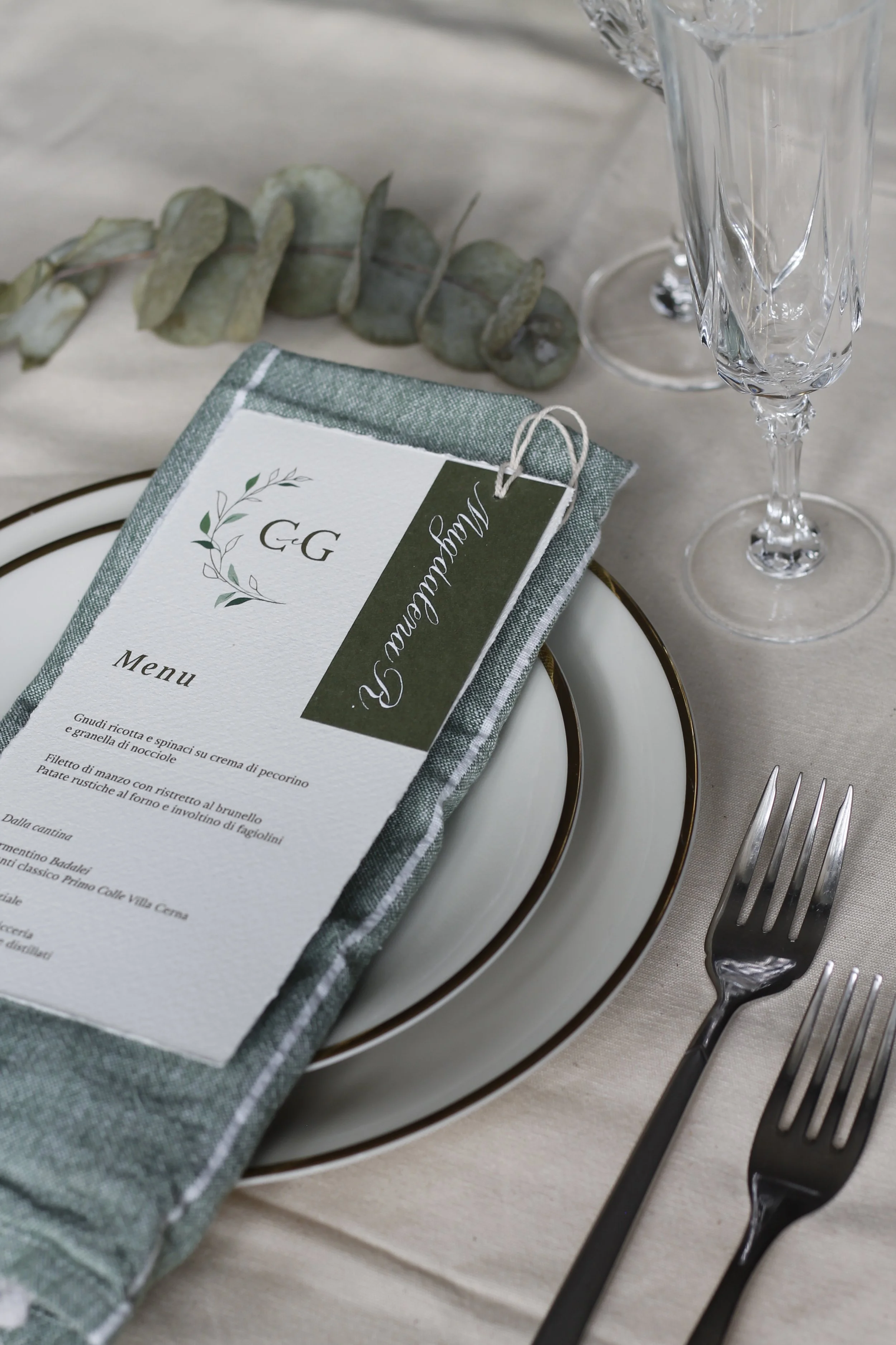 Tavola apparecchiata con piatti, forchette, calici di vetro, tovagliolo e menù di nozze.