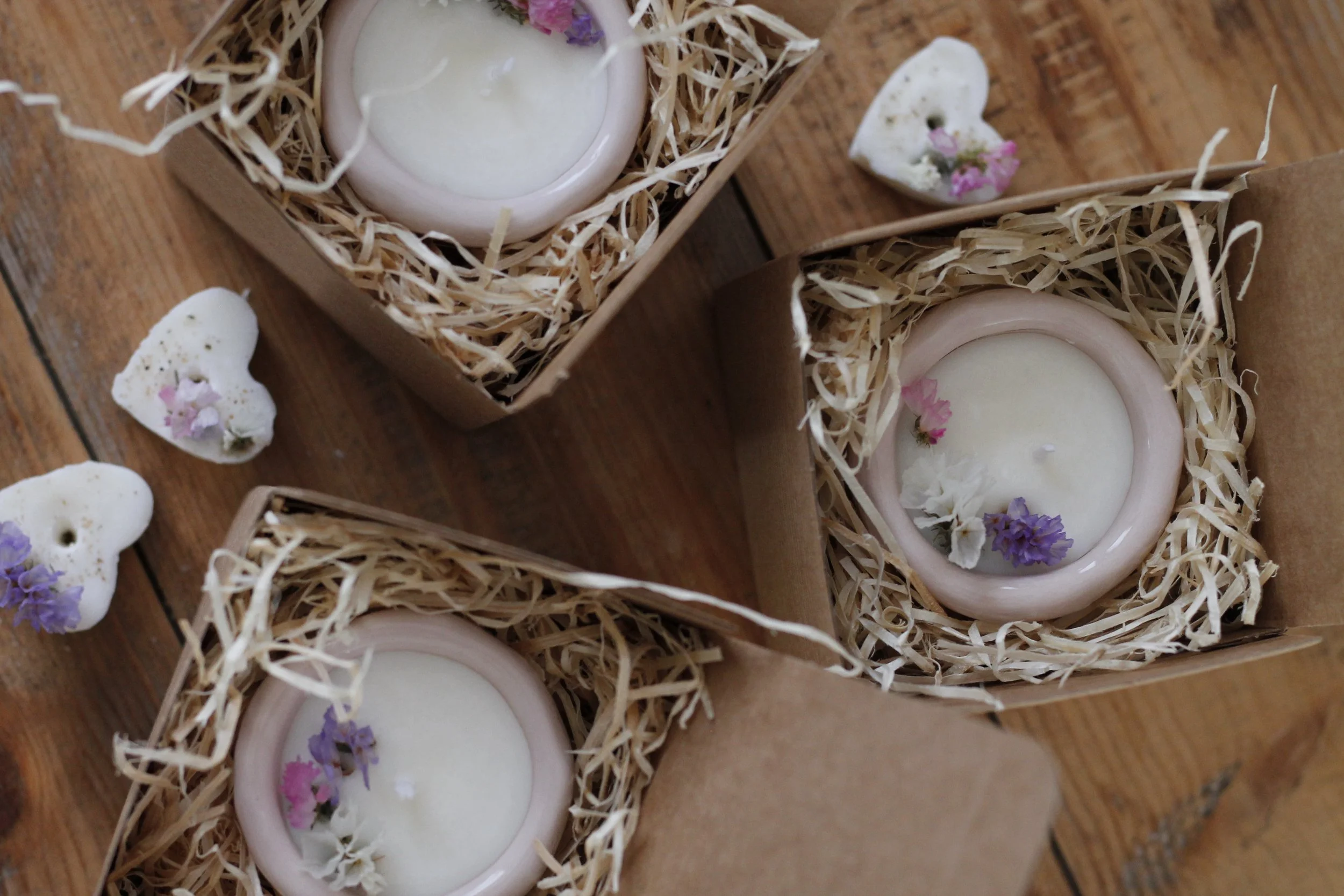 Candele bianche in scatole di cartone con decorazioni di fiori secchi e petali, sul tavolo di legno.
