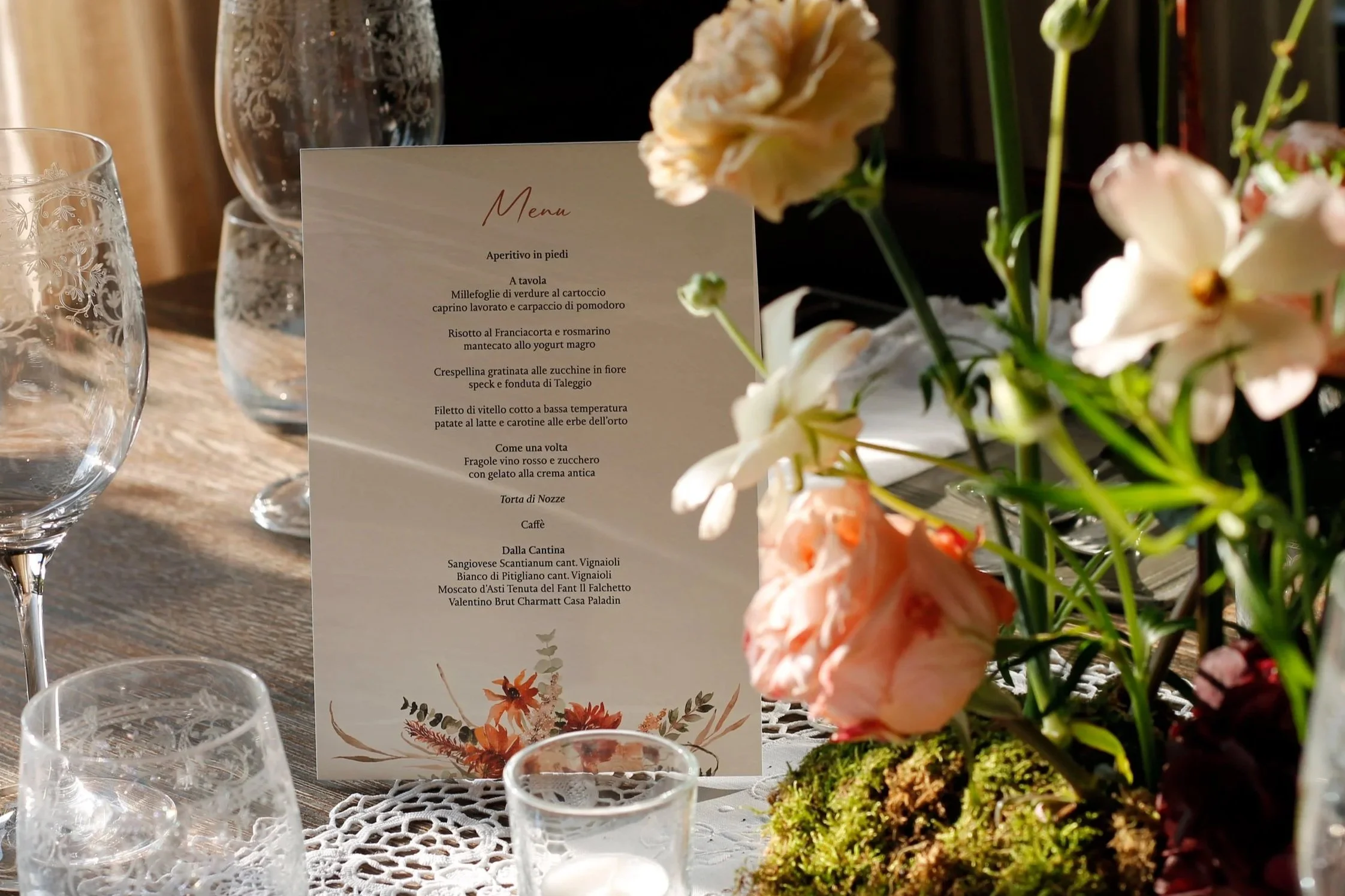 Menù in primo piano con fiori freschi e bicchieri di vetro su una tovaglia ricamata.