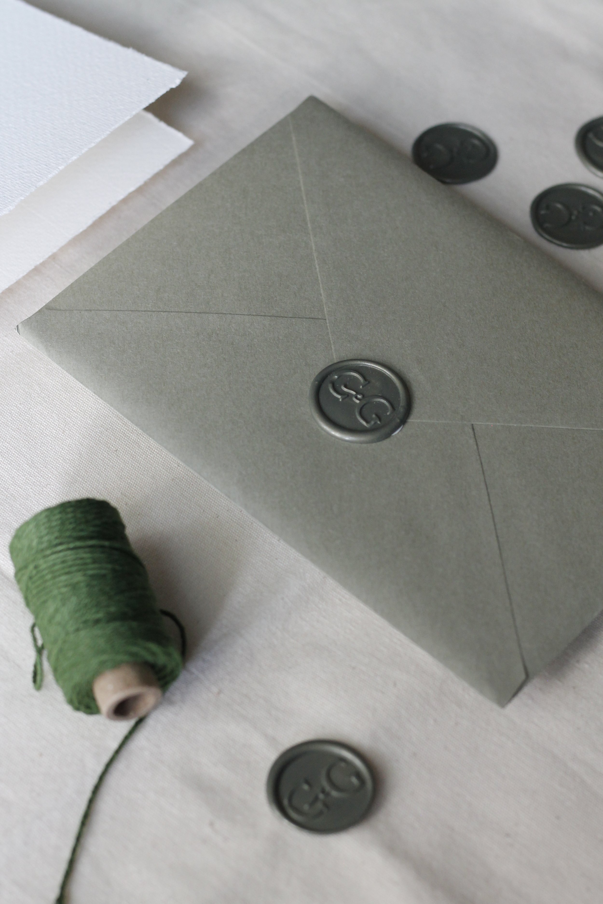 Scatola grigia con ceralacca, fogli di carta bianca e carta grigia, spago verde e ceralacca, e alcuni occhielli di metallo.