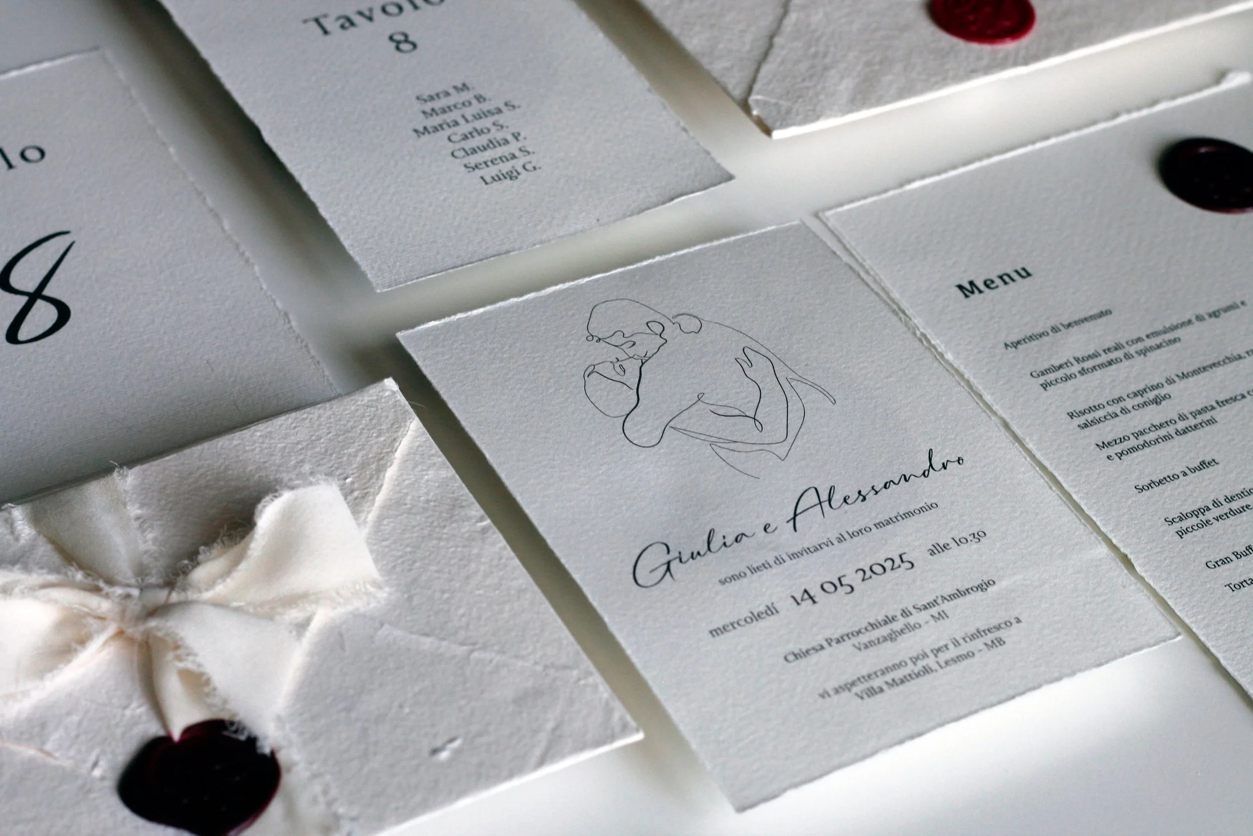 Inviti di nozze con un disegno stilizzato di una coppia che si bacia, dettagli di menù, e biglietti di ringraziamento con un fiocco e bacca di gelso.