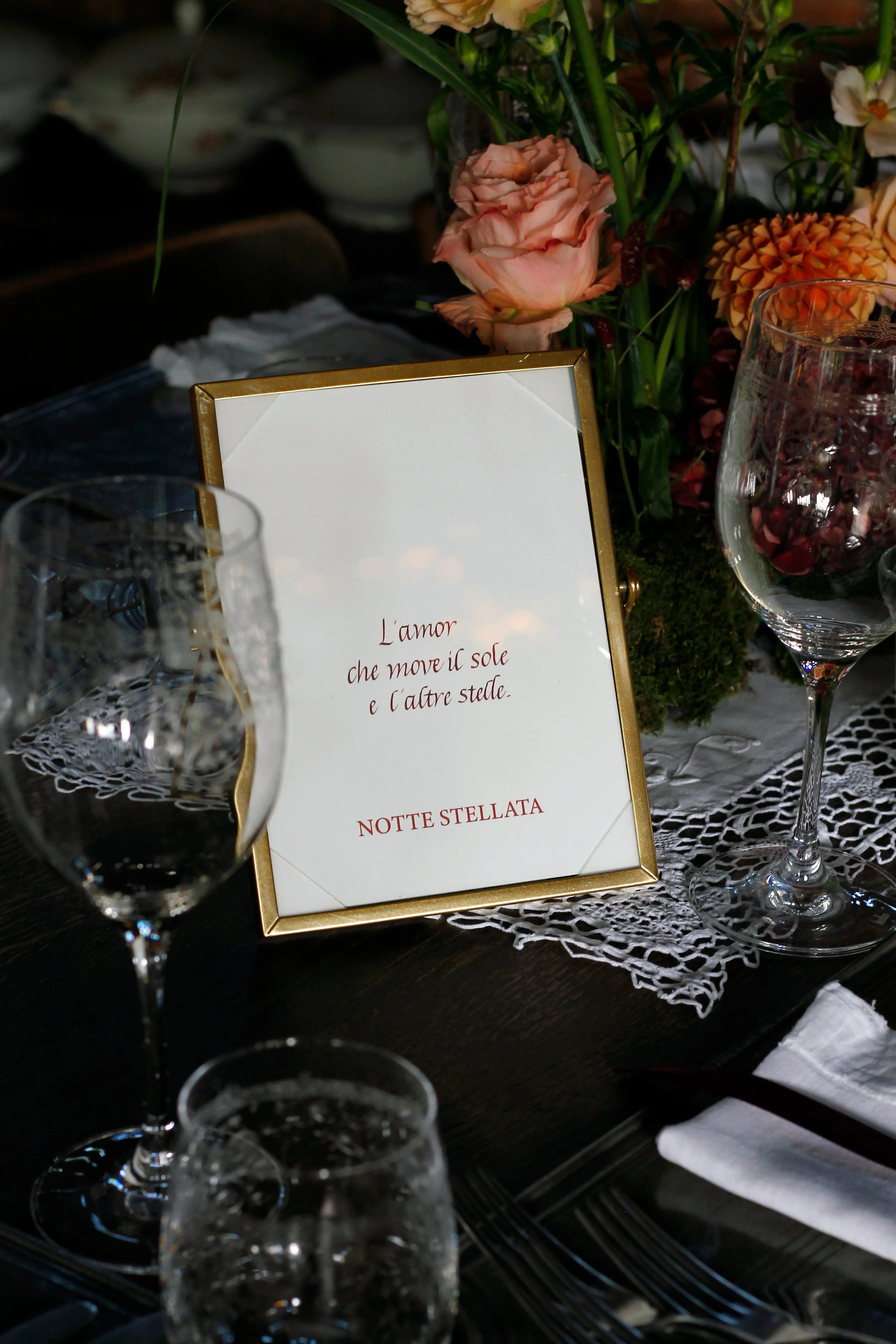 Tavola imbandita con bicchieri e un centrotavola di fiori, con un cartellino con scritta in italiano.